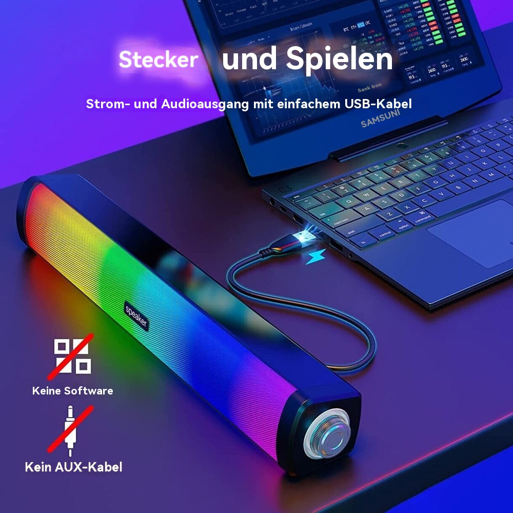 Ein Lautsprecher mit Regenbogenverlauf, per USB-Kabel mit einem Laptop verbunden, auf einem dunklen Schreibtisch.