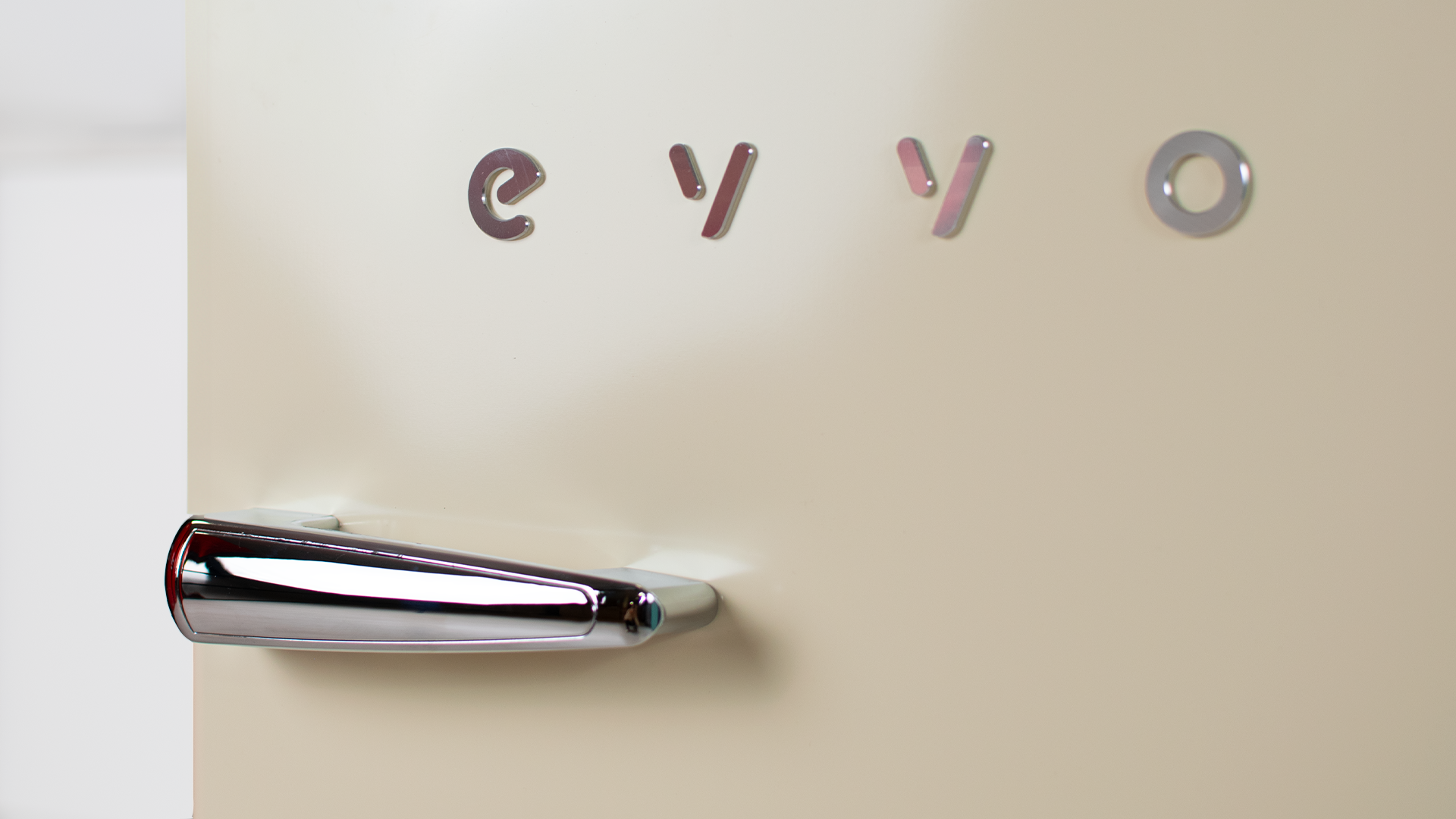 Primer plano de puerta de nevera beige con letras 'evvo' y asa plateada. Fondo claro.