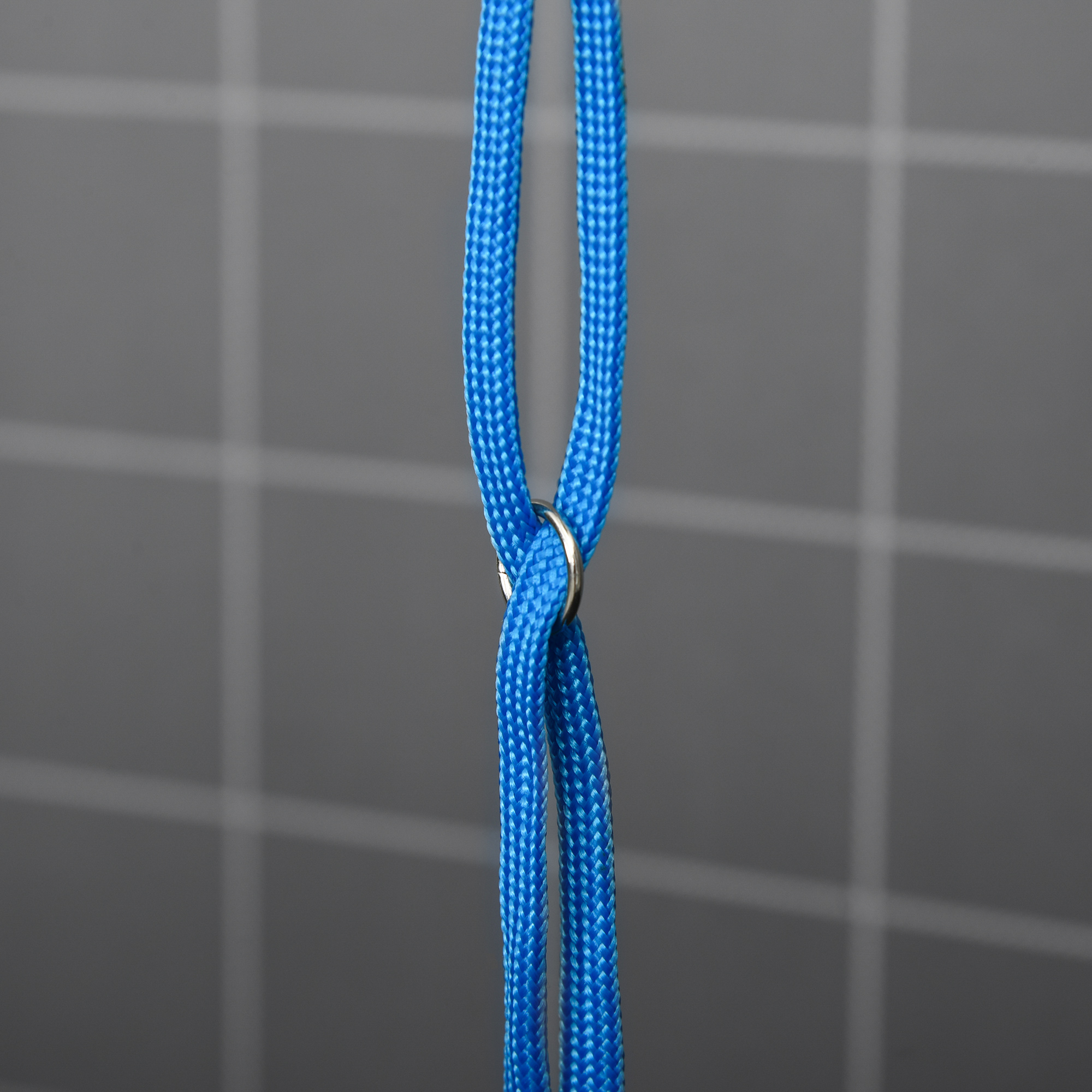 Nahaufnahme eines blauen Seils mit Metallring in der Mitte, vor kariertem Hintergrund.