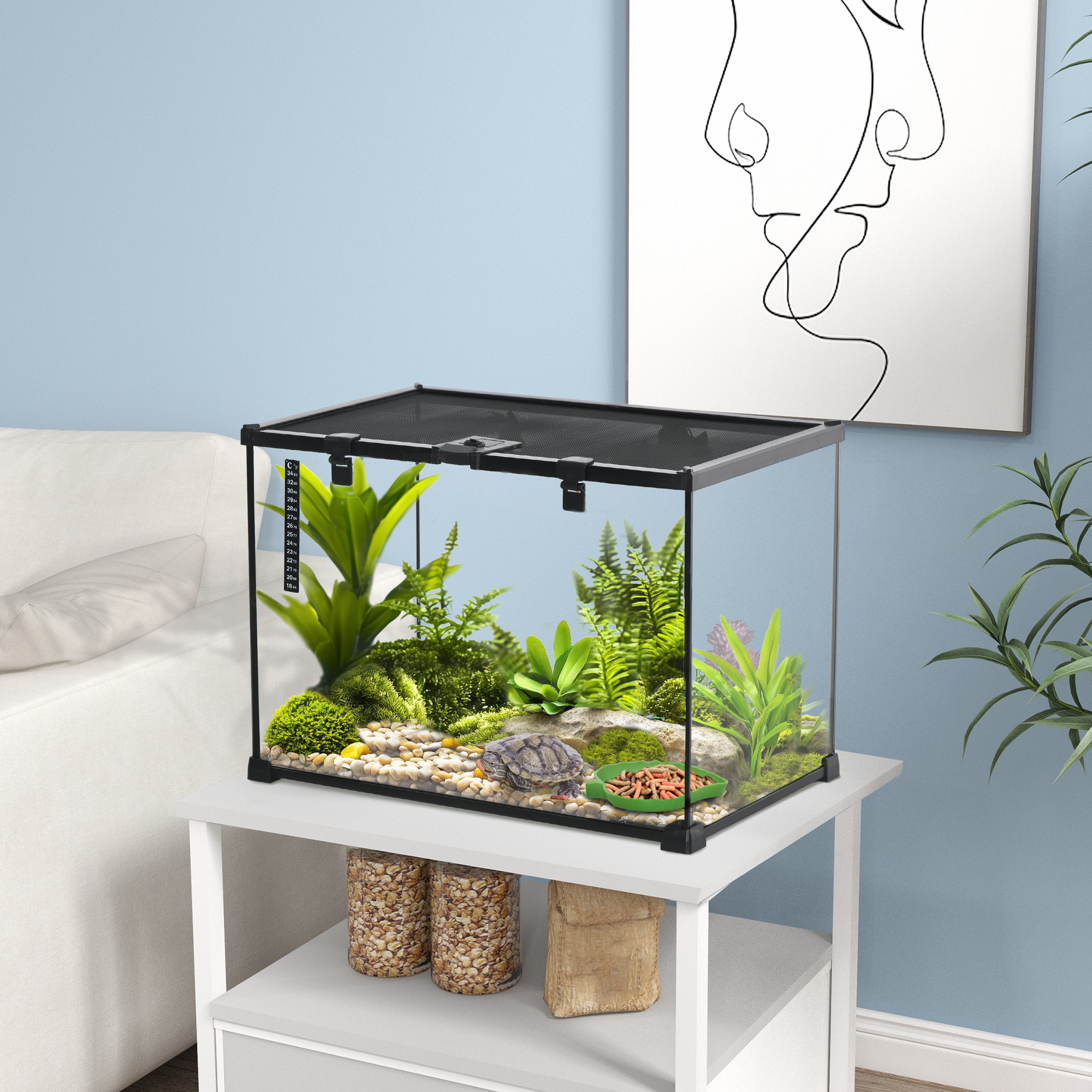 Terrariumeinrichtung mit Pflanzen, einer Schildkröte und einer blattförmigen Schale, auf einem weißen Tisch.