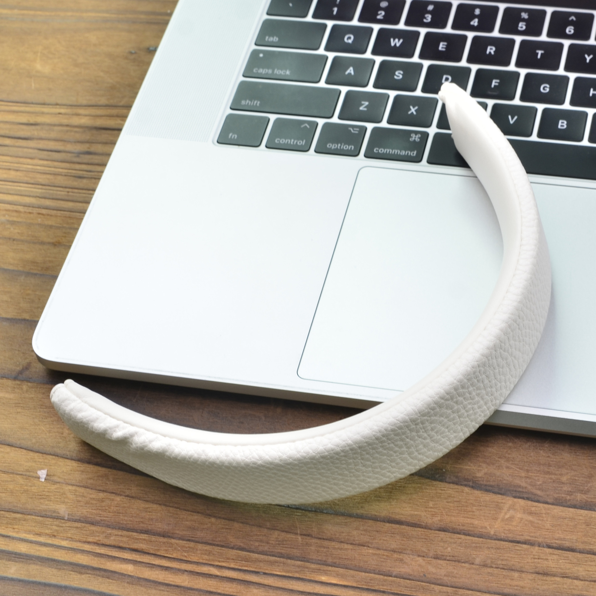Una fascia bianca per cuffie poggia su un laptop argentato, su un tavolo di legno.