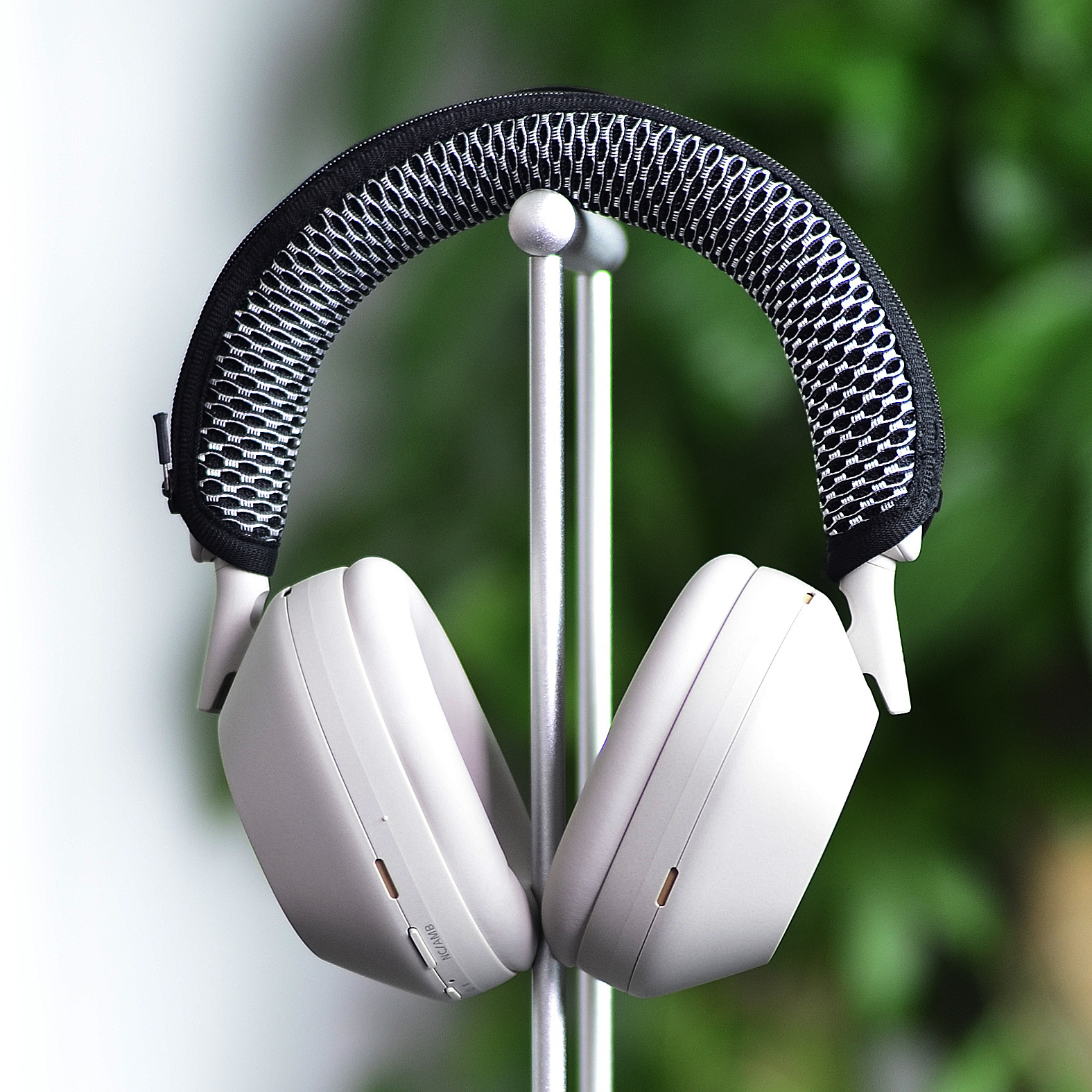 Słuchawki na stojaku z czarno-białym pałąkiem, przed zieloną rośliną.
