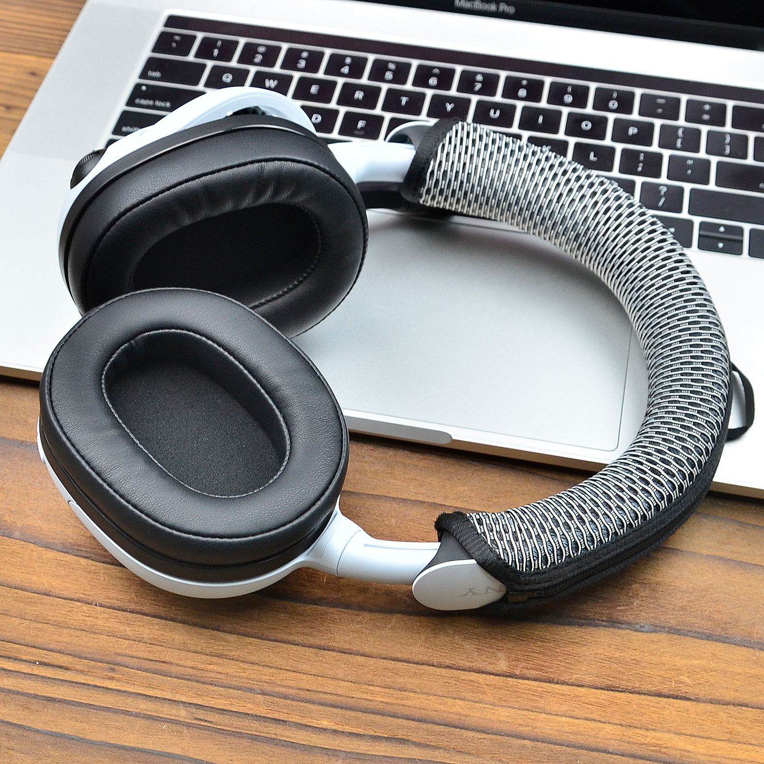 Białe słuchawki z czarnymi nausznikami na laptopie. Pałąk jest pokryty szaro-białą, teksturowaną tkaniną.