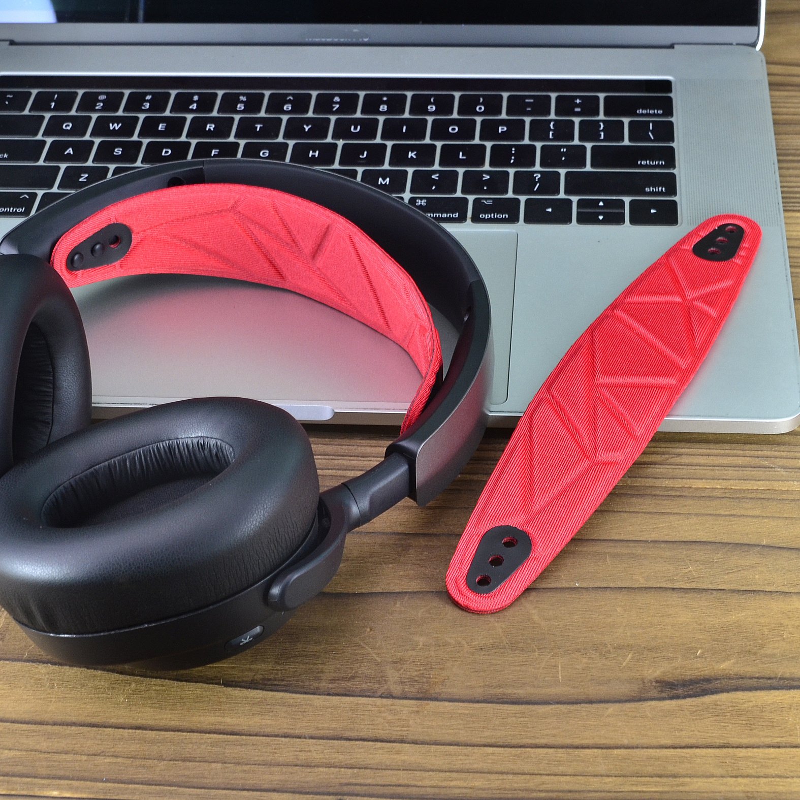 Cuffie nere su un laptop. Un rivestimento rosso per la fascia e un pezzo rosso staccato su legno.