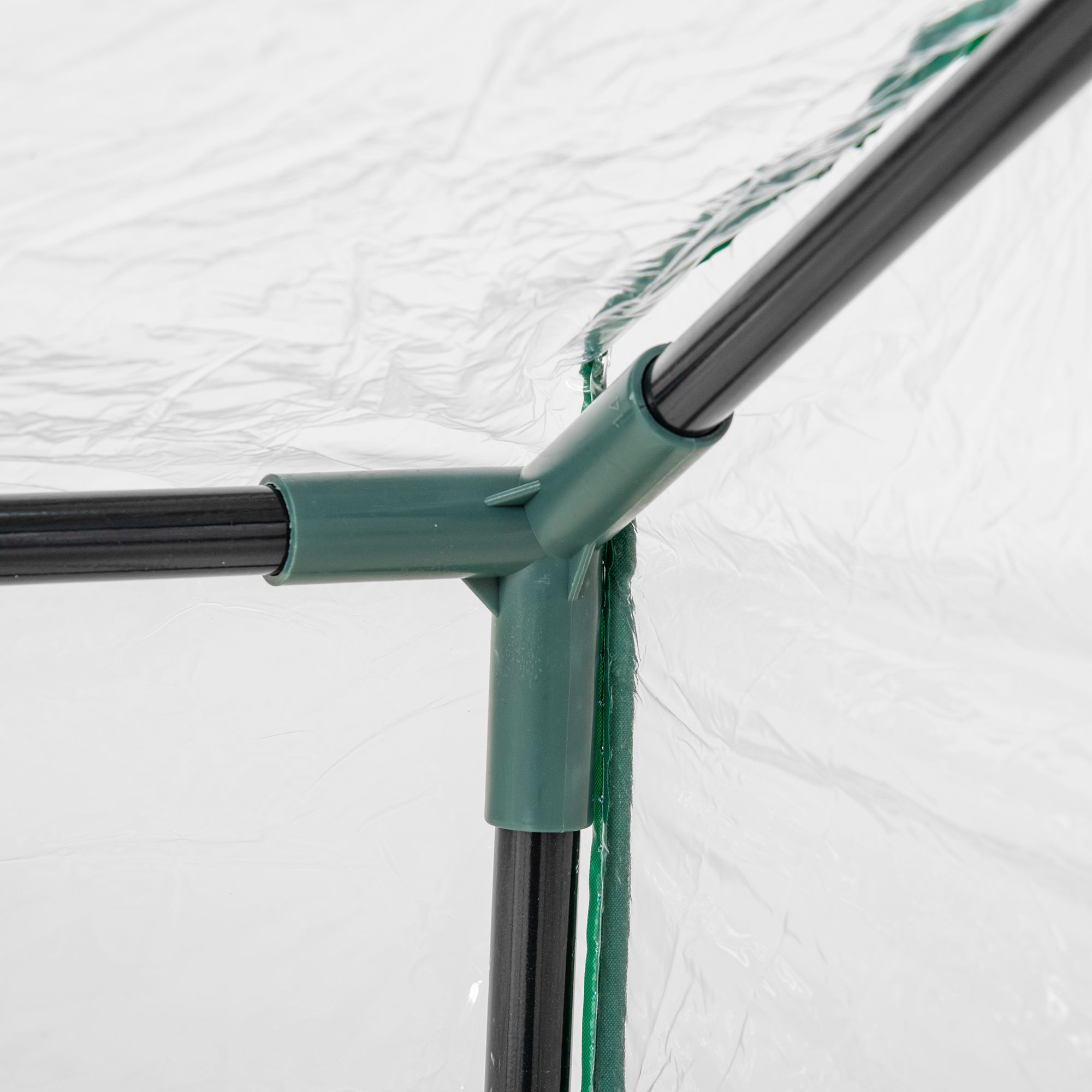 Vista de cerca de una unión de invernadero. Conector de plástico verde y marco de metal negro. Cubierta de plástico blanco.