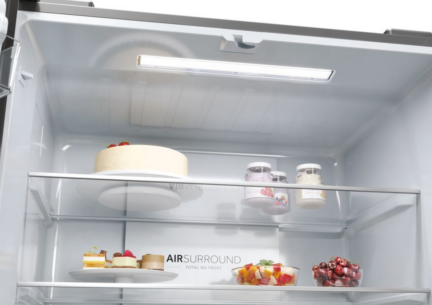 Interno frigorifero con torta, barattoli e frutta. Luce sopra e ripiani in vetro.