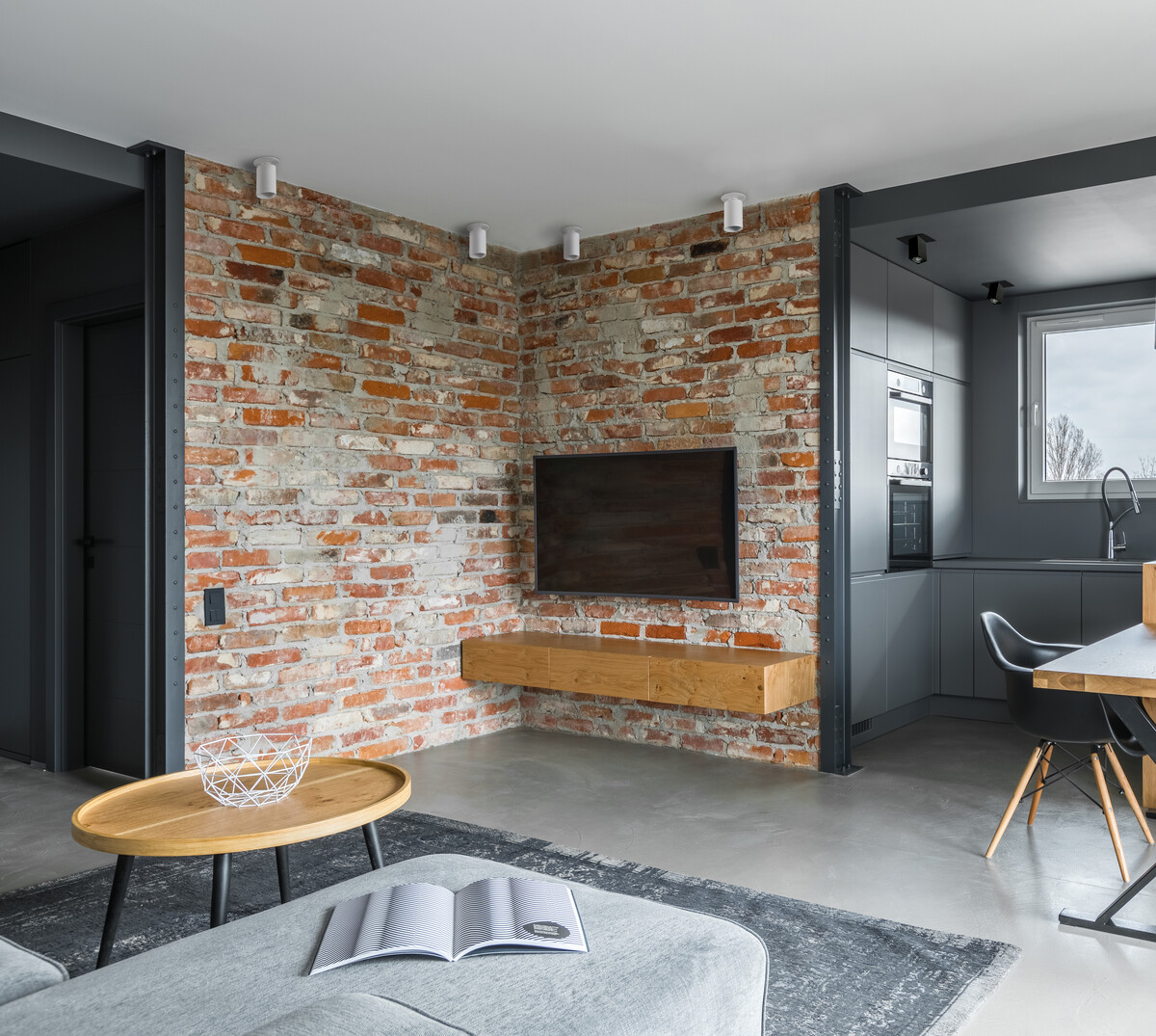 Interni: Muro di mattoni con TV, mensola galleggiante in legno, divano grigio e tappeto. Design moderno.