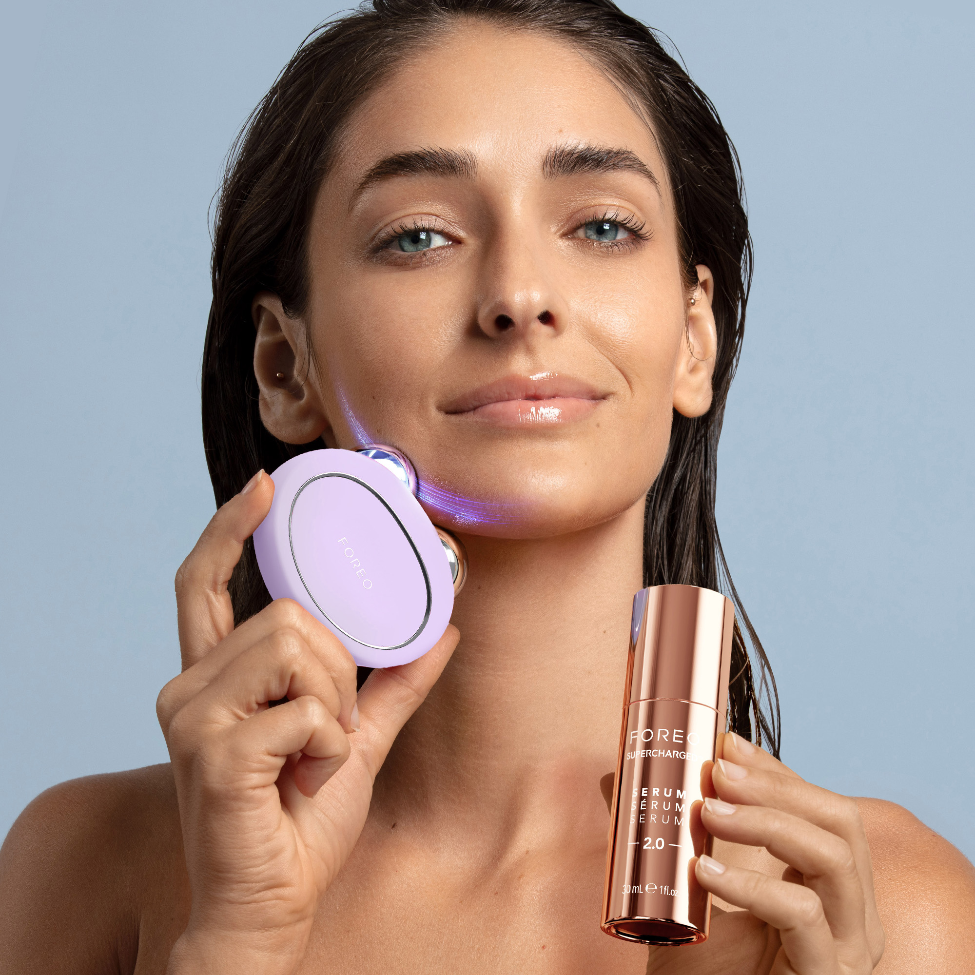 Femme tenant un appareil Foreo et une bouteille de sérum.