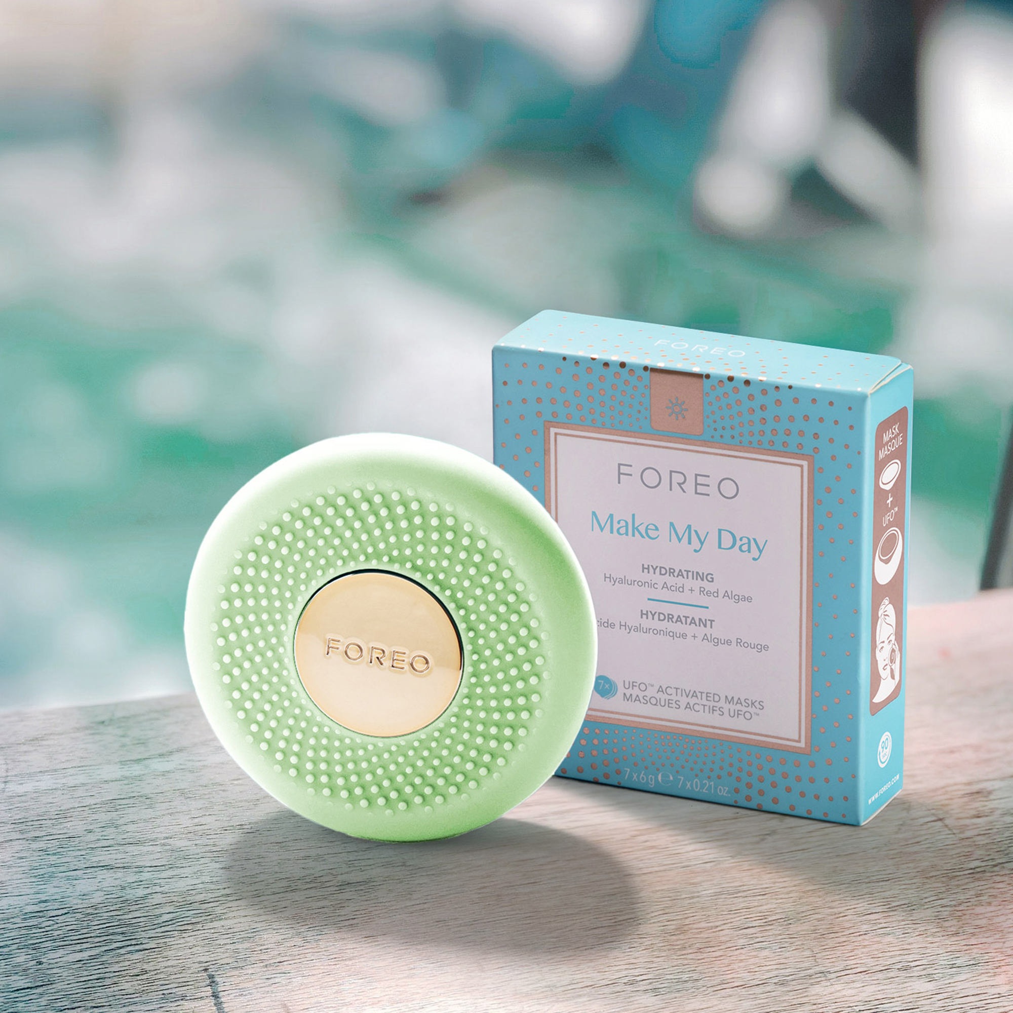 Groen Foreo-apparaat en maskerverpakking op hout bij zwembad. Productfoto met tekst: 'Make My Day'.