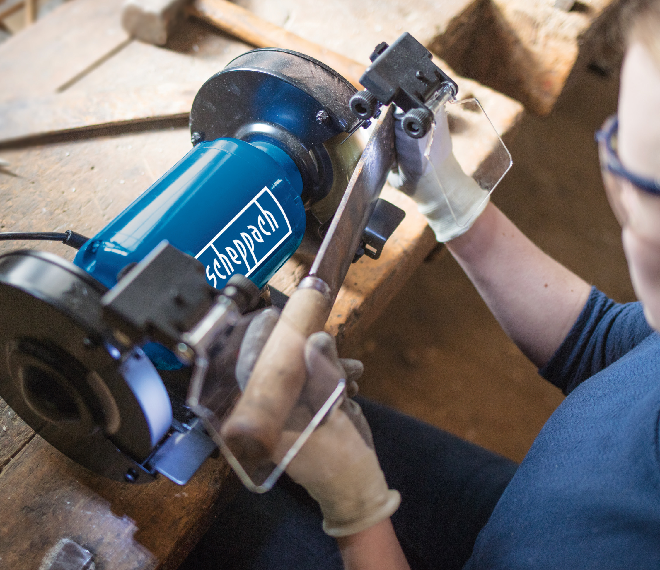 Osoba używa szlifierki. Ma na sobie rękawice i okulary ochronne, ostrząc ostrze.
