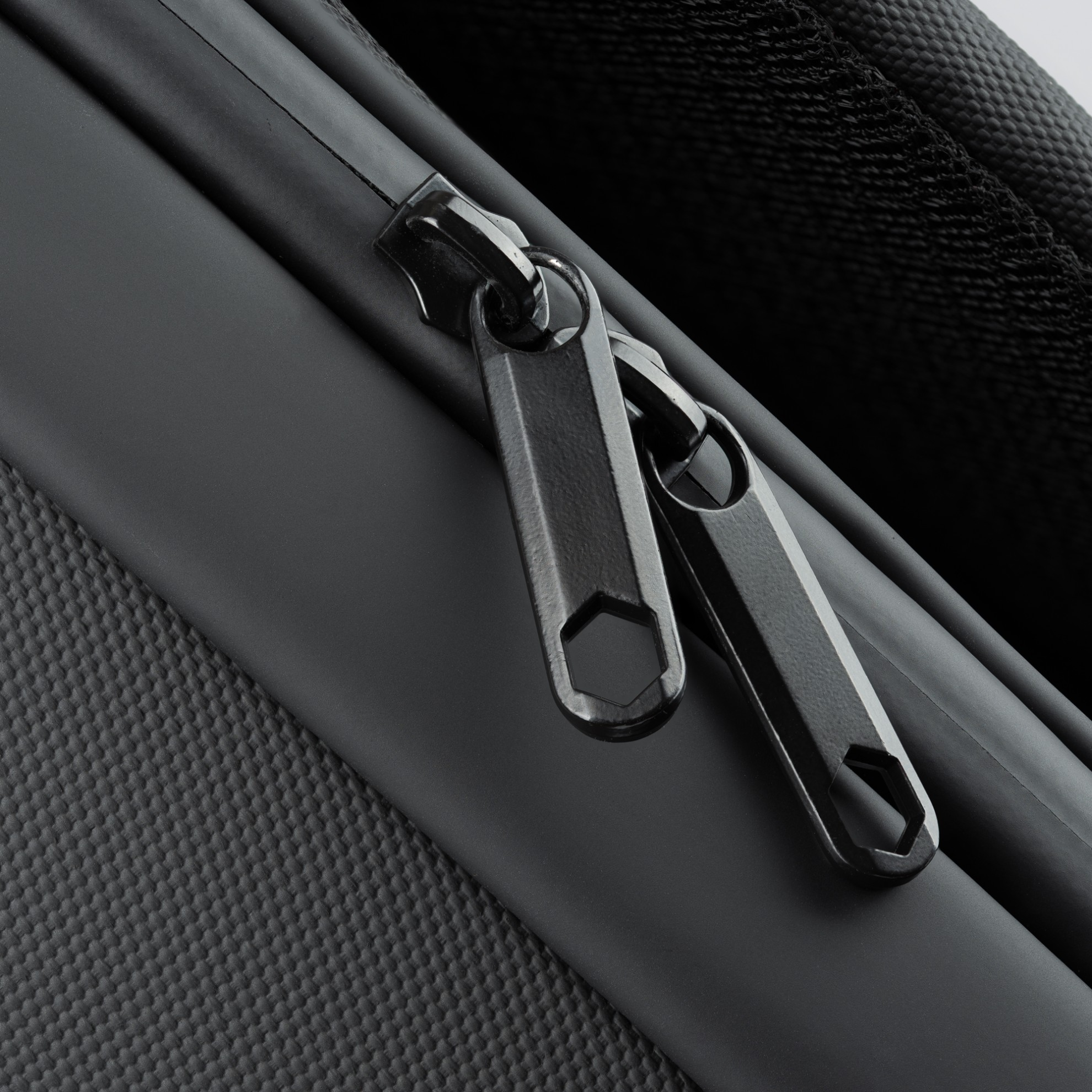 Zbliżenie na zamek błyskawiczny czarnego plecaka. Widoczne są dwa czarne suwaki.