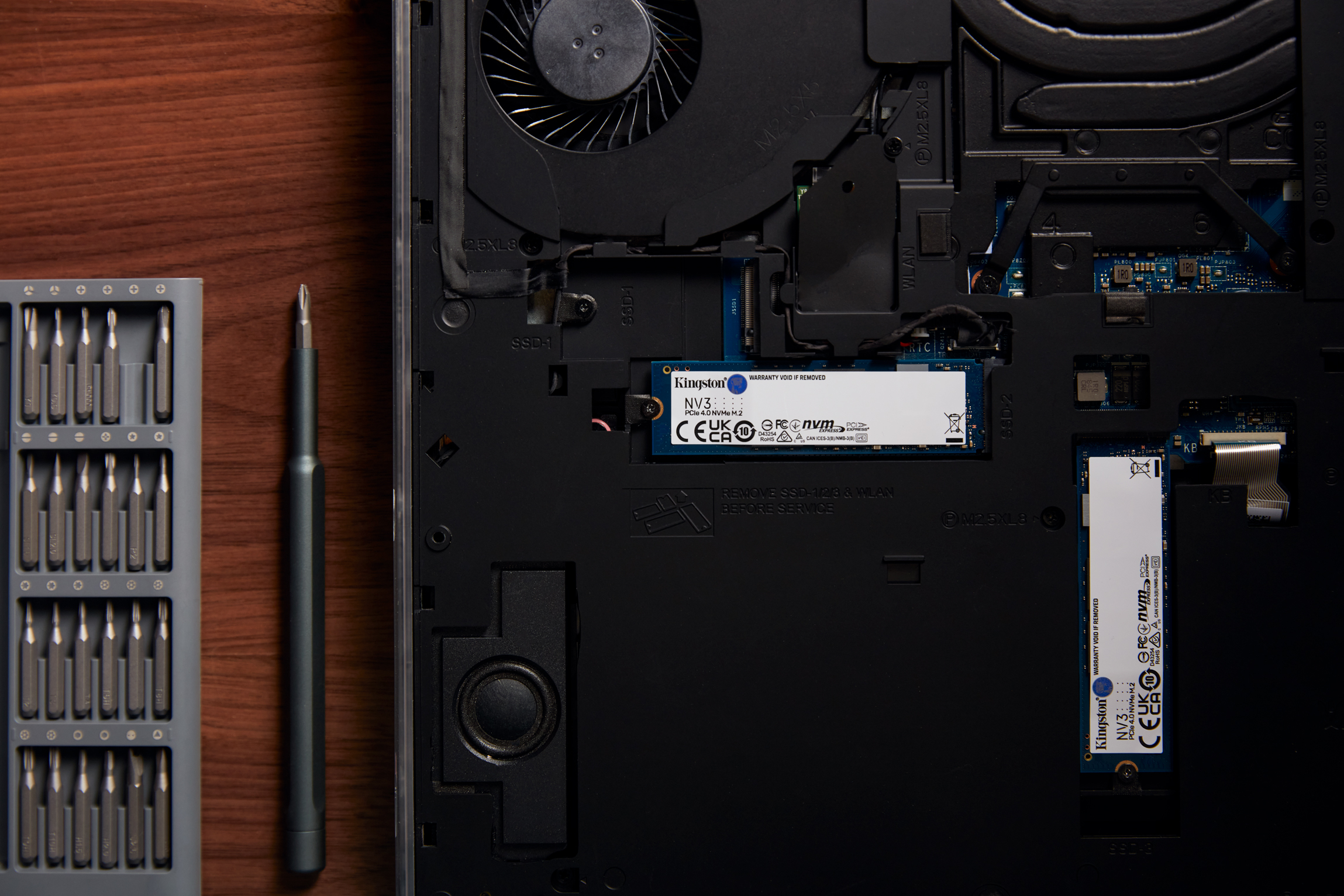 Un portátil abierto, con instalación de SSD y herramientas sobre una superficie de madera.