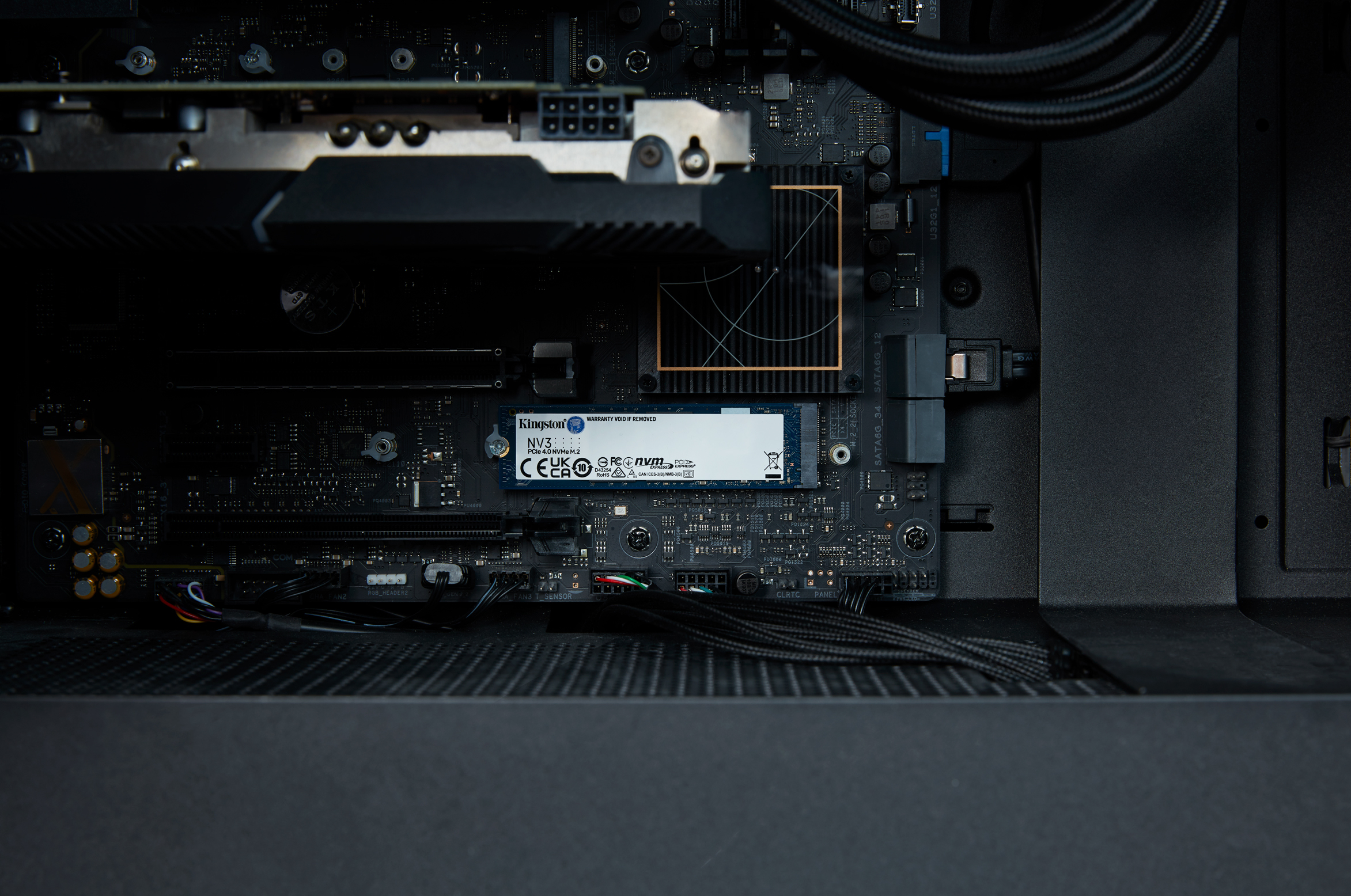 Dentro de la caja de la computadora: SSD Kingston NV3, placa base, cables, fondo oscuro.