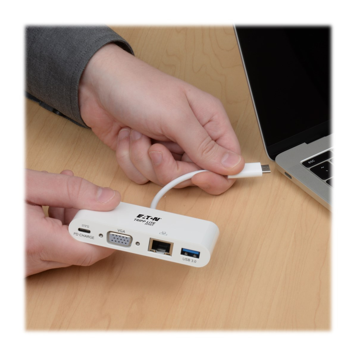 Una persona tiene un hub USB-C bianco vicino a un laptop su una superficie di legno.