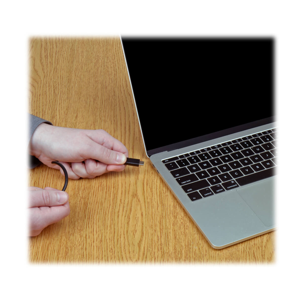 Osoba podłączająca kabel USB-C do laptopa na drewnianym stole.