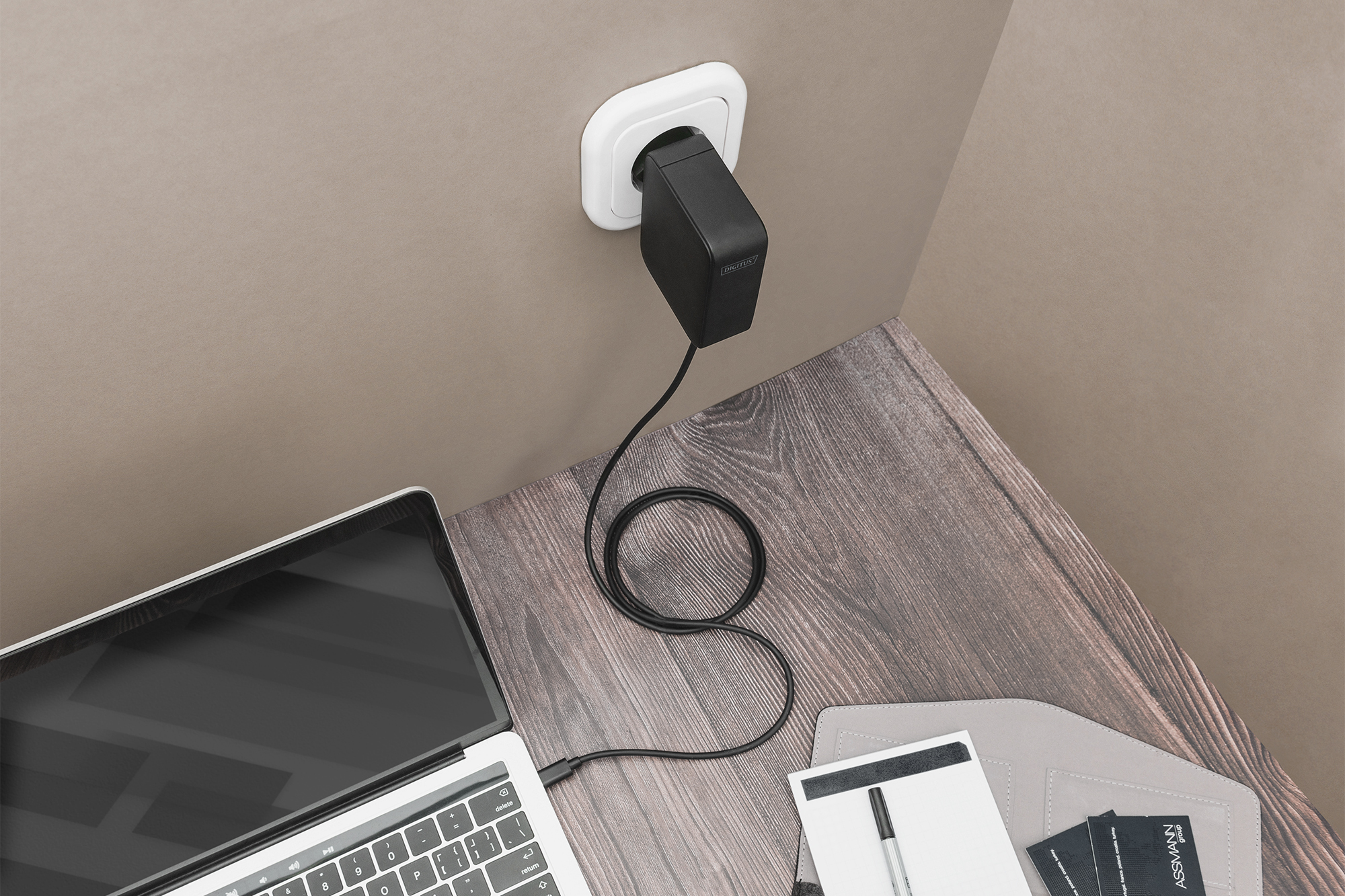 Caricabatterie per laptop nero collegato a una presa a muro. Connesso a un laptop su una scrivania.