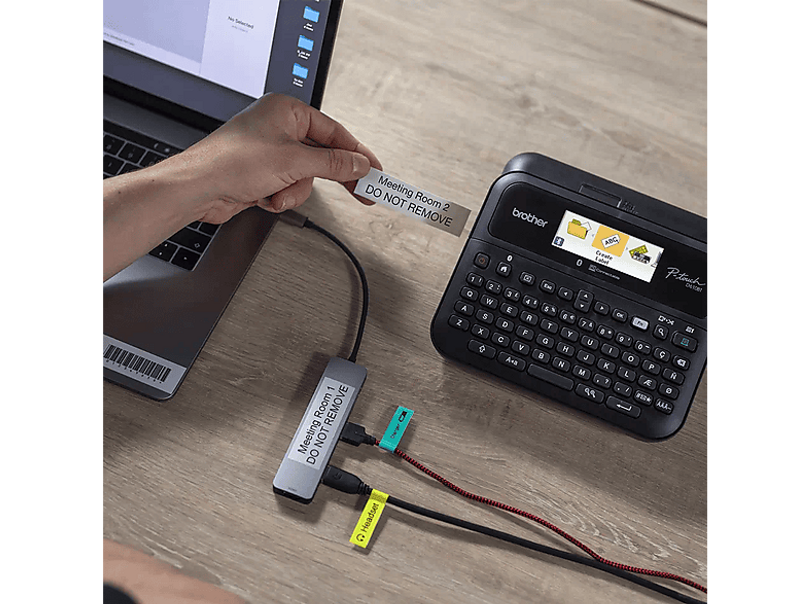 Osoba etykietująca kable za pomocą drukarki, laptopa i etykiet na drewnianym stole.