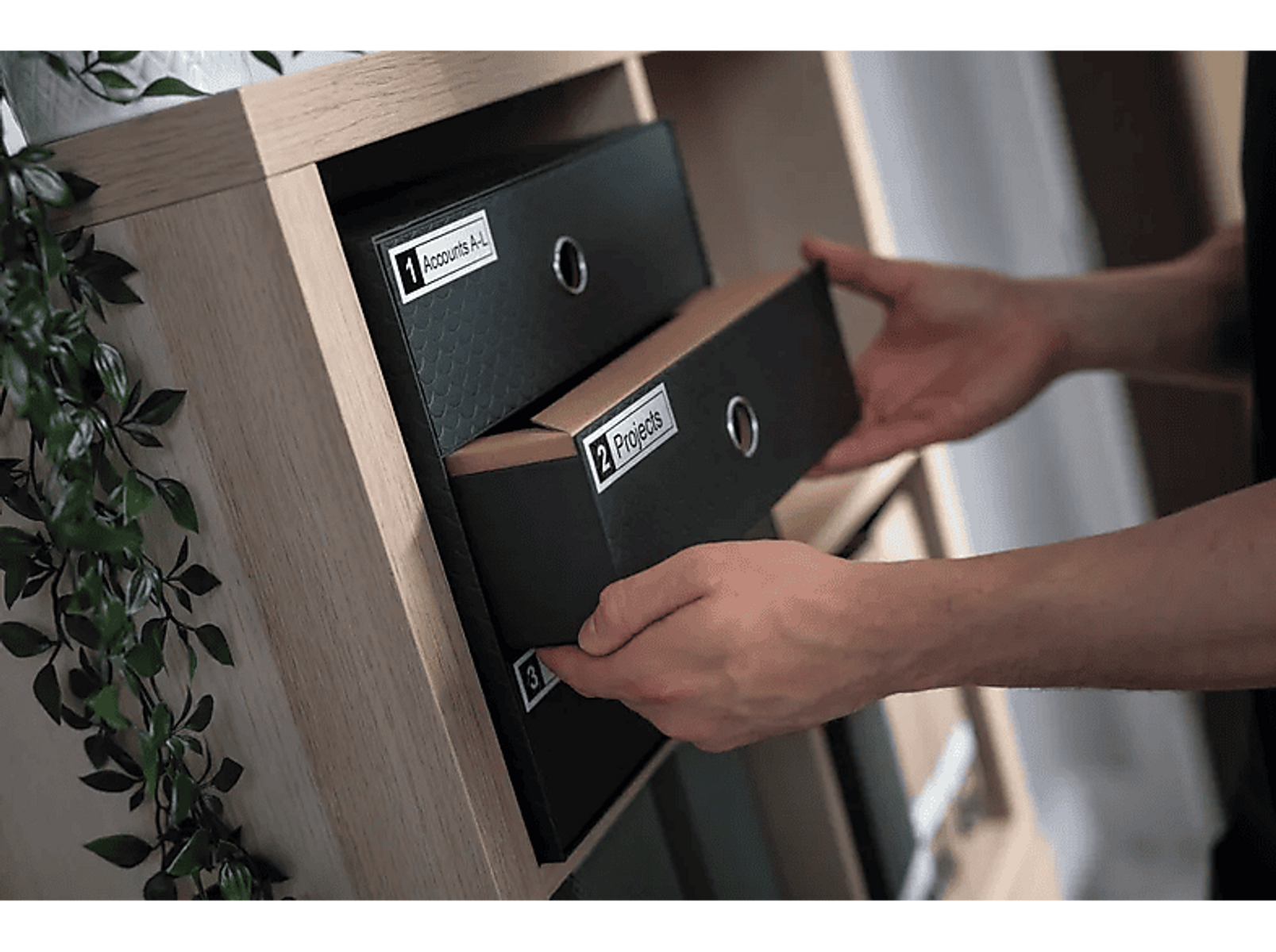 Ręce otwierające szuflady z etykietami. Szuflady są oznaczone 'Accounts A-L' i 'Projects'.
