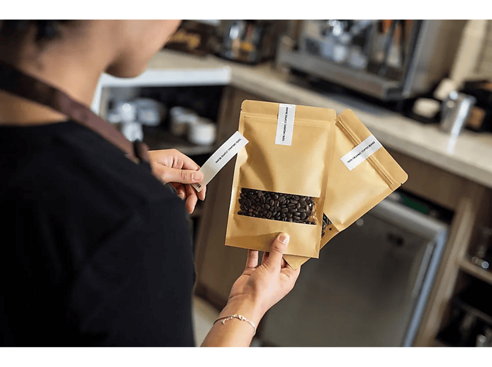 Osoba trzymająca etykietowane worki z ziarnami kawy przed kawiarnią.