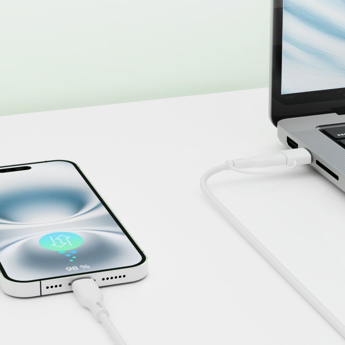Telefon ładujący się białym kablem, podłączony do laptopa na białym biurku.