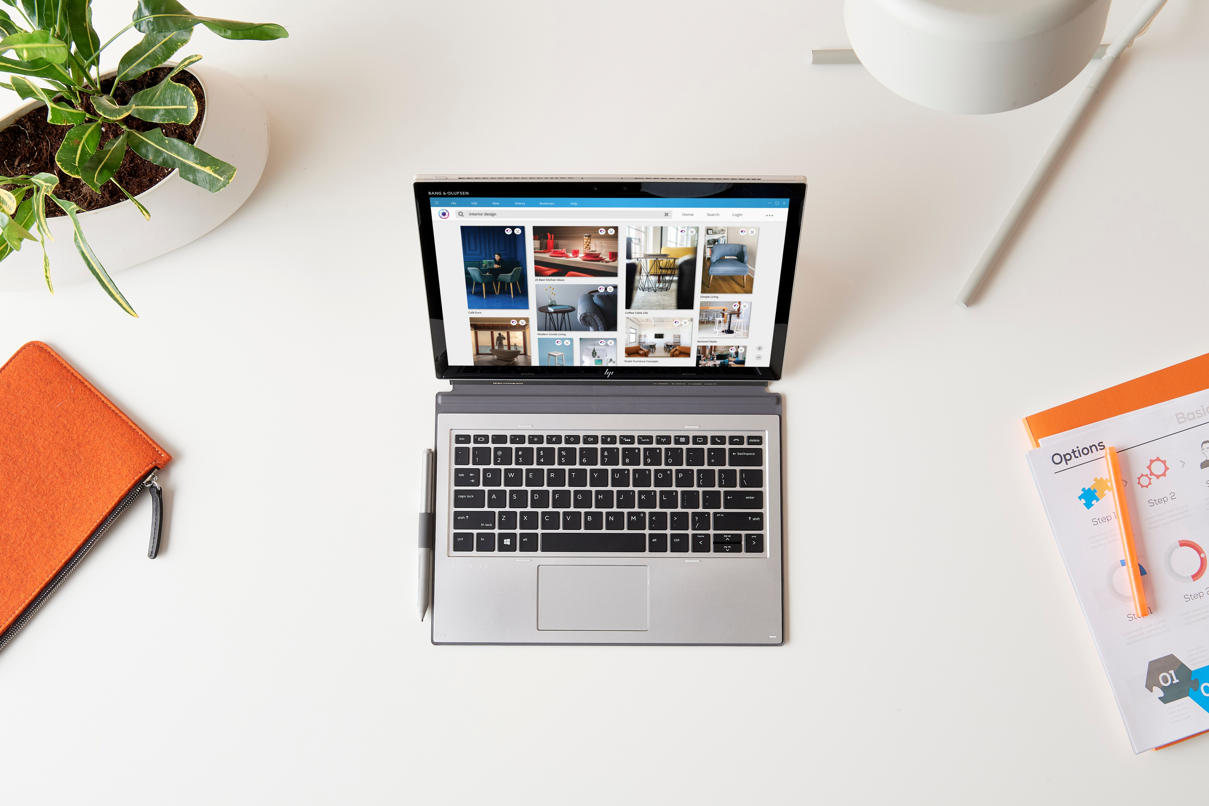 Laptop ze stroną internetową na ekranie, długopisem i notatnikiem, białe tło.