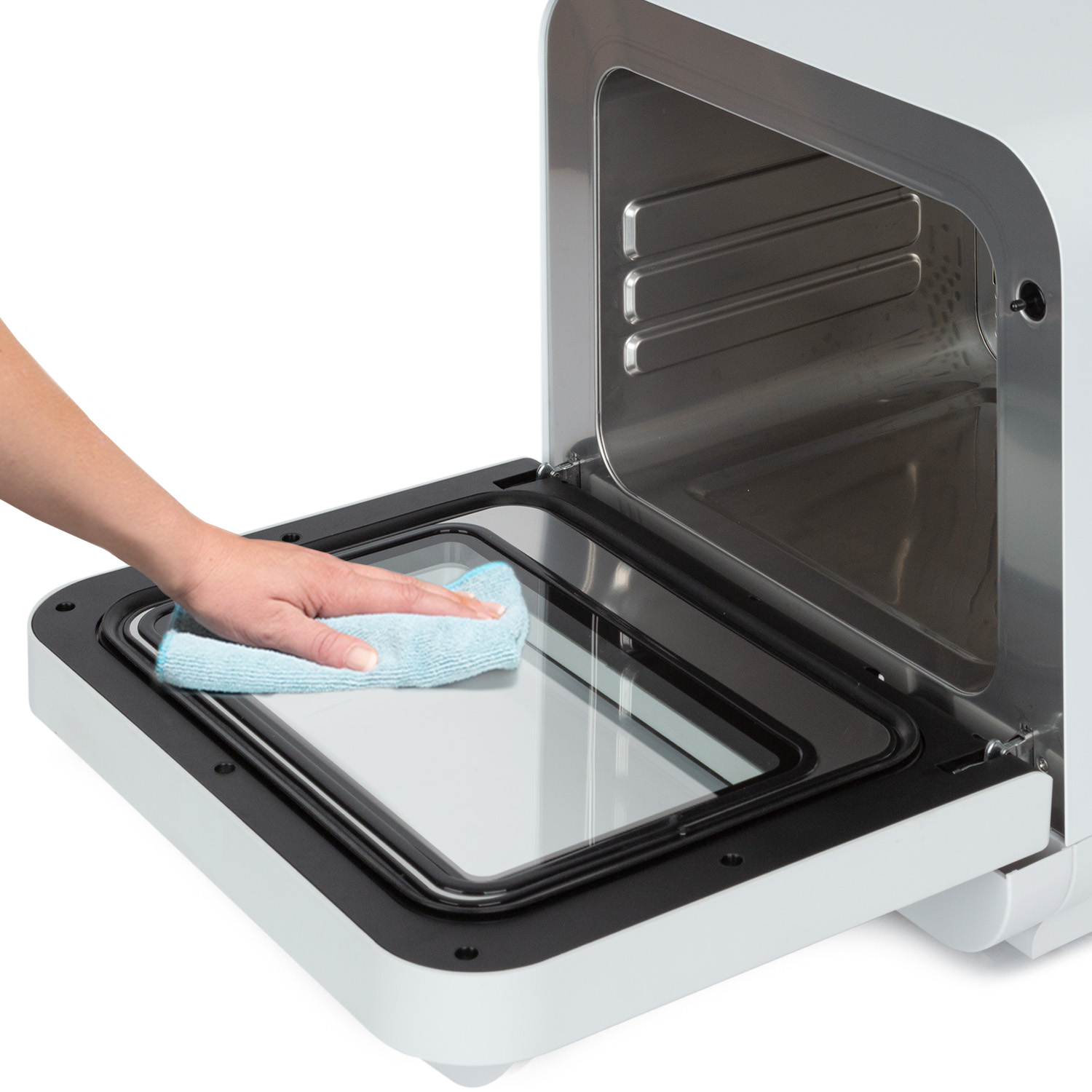 Una mano pulisce il vetro di una porta del forno con un panno blu, all'interno di un forno bianco.