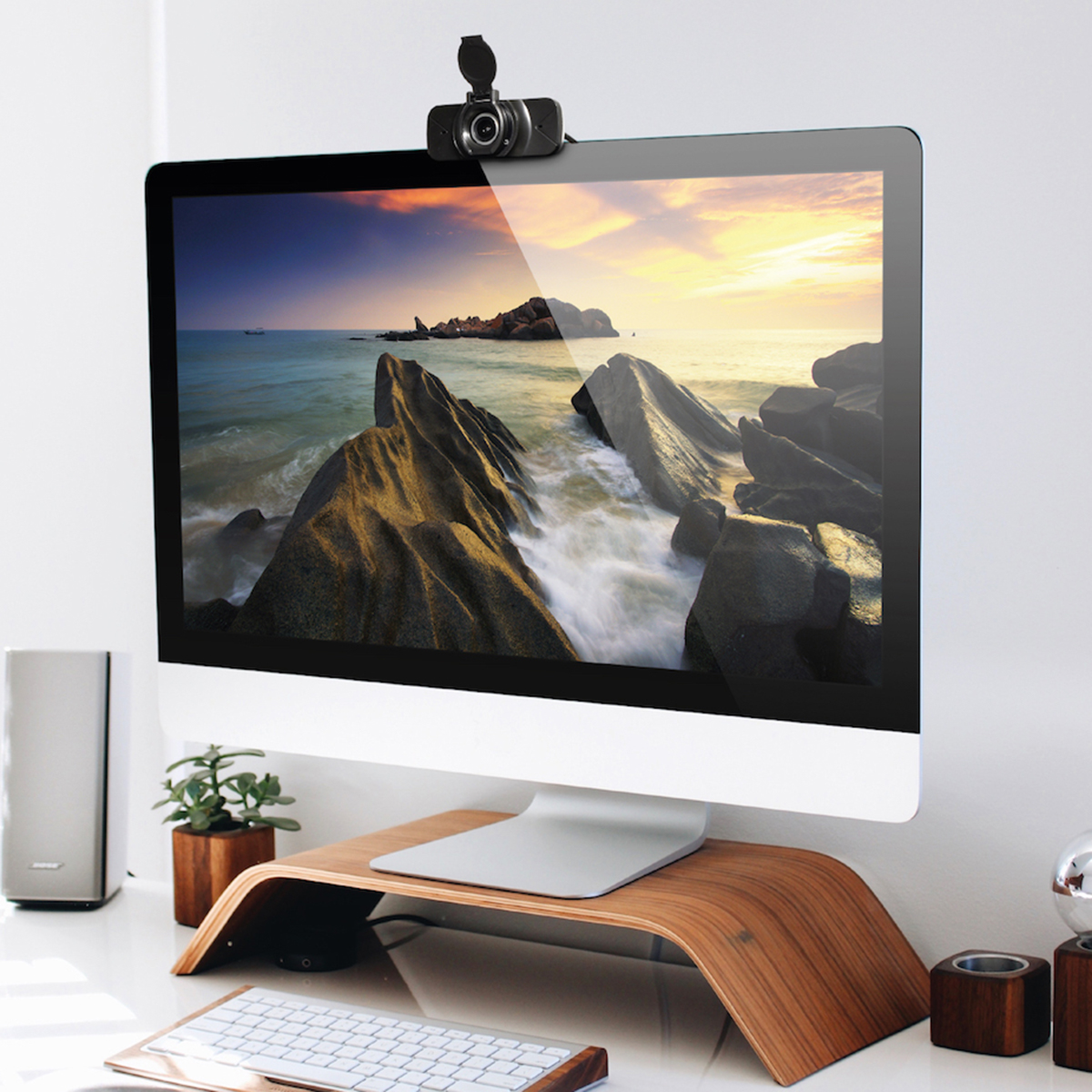 Monitor komputera z kamerą internetową na górze, skały w morzu i drewniany stojak na biurko.