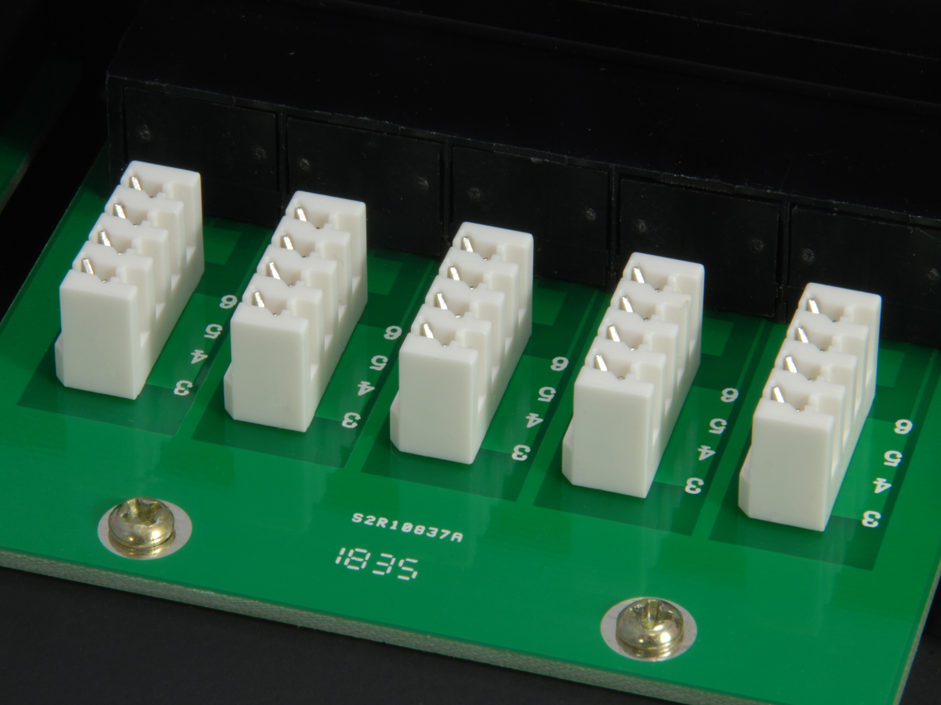 Zbliżenie zielonej płytki drukowanej z białymi prostokątnymi złączami i czarnym elementem.