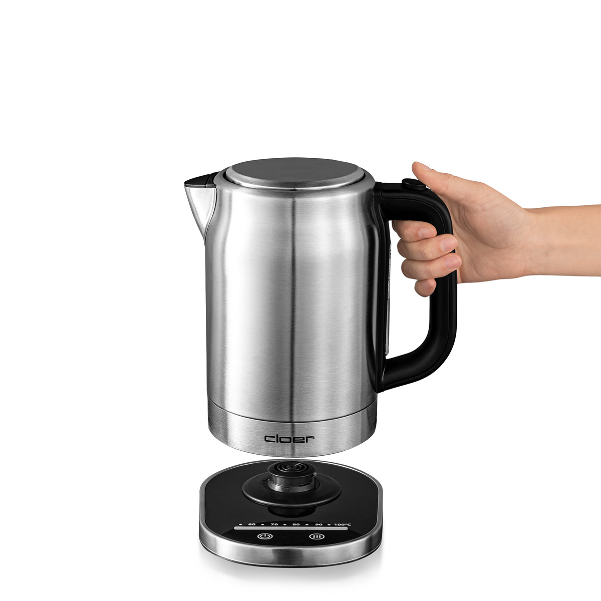 Czajnik podnoszony z podstawy. Ręka trzyma czajnik, podstawa wciąż na stole.