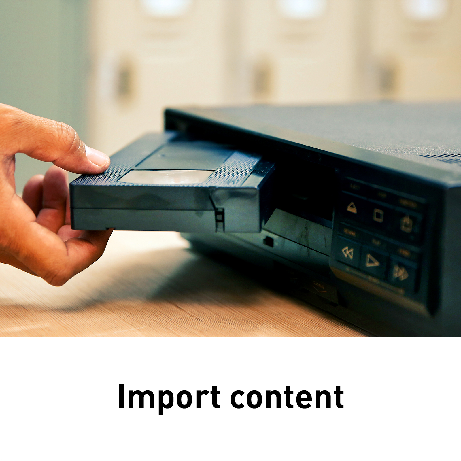 Ręka wkładająca kasetę VHS do czarnego magnetowidu. Tekst 'Importuj zawartość'.