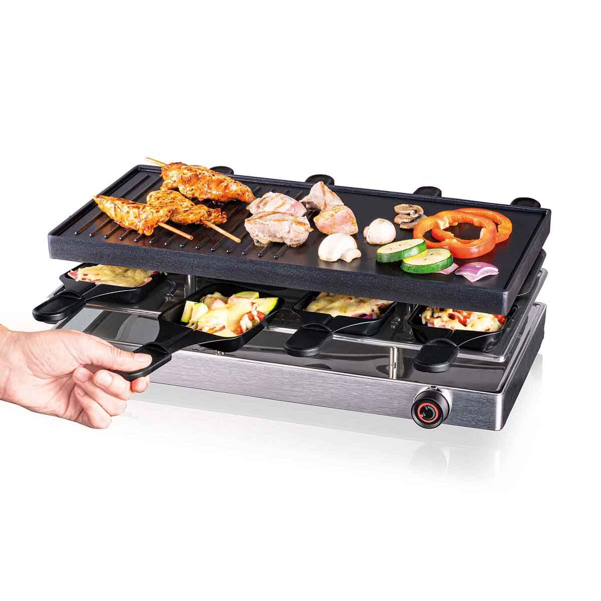 Una griglia per raclette con cibo è mostrata. Carne e verdure grigliate sono in cima e il formaggio si scioglie sotto.