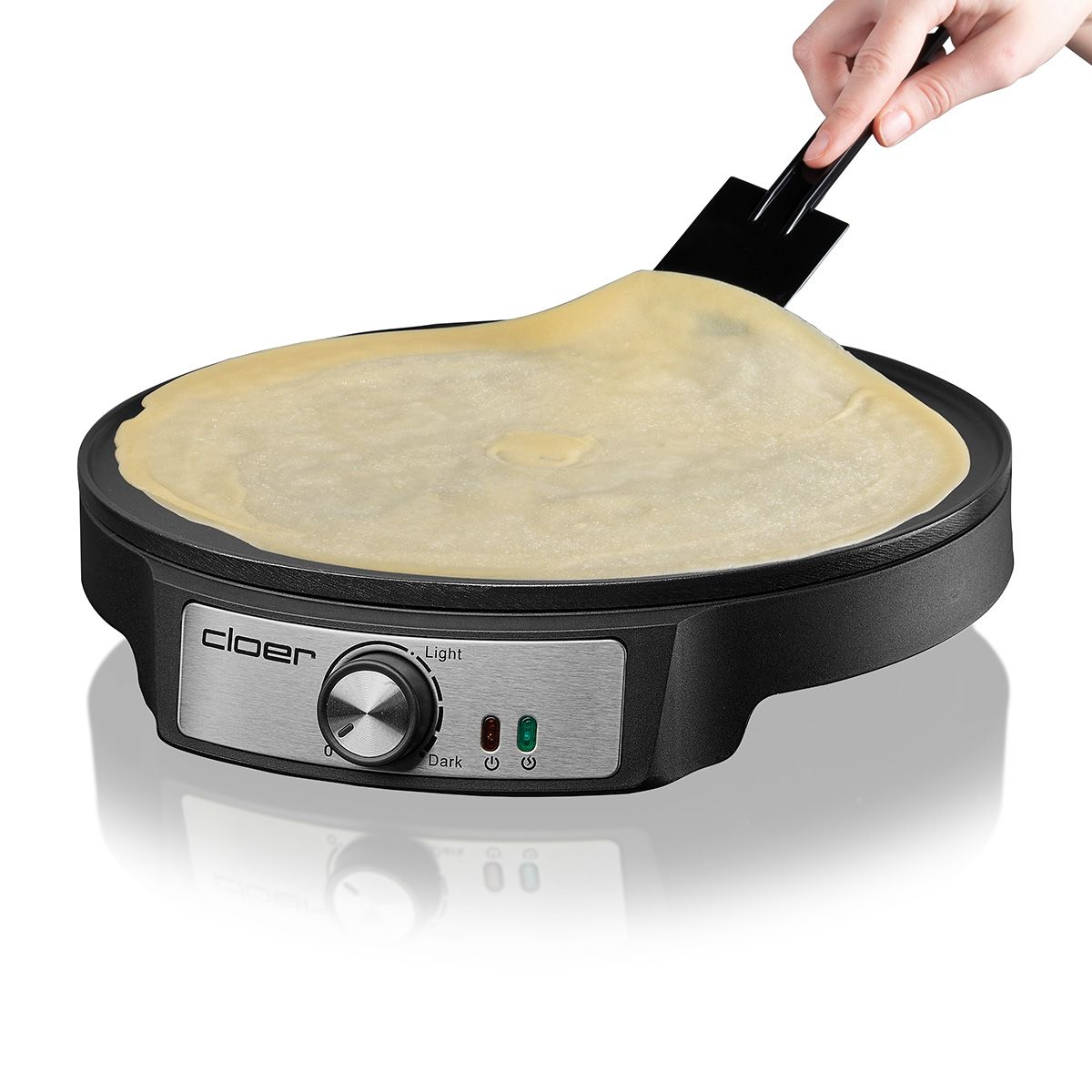 Macchina per crepe con una crepe sopra. Una mano usa una spatola. Sfondo bianco.