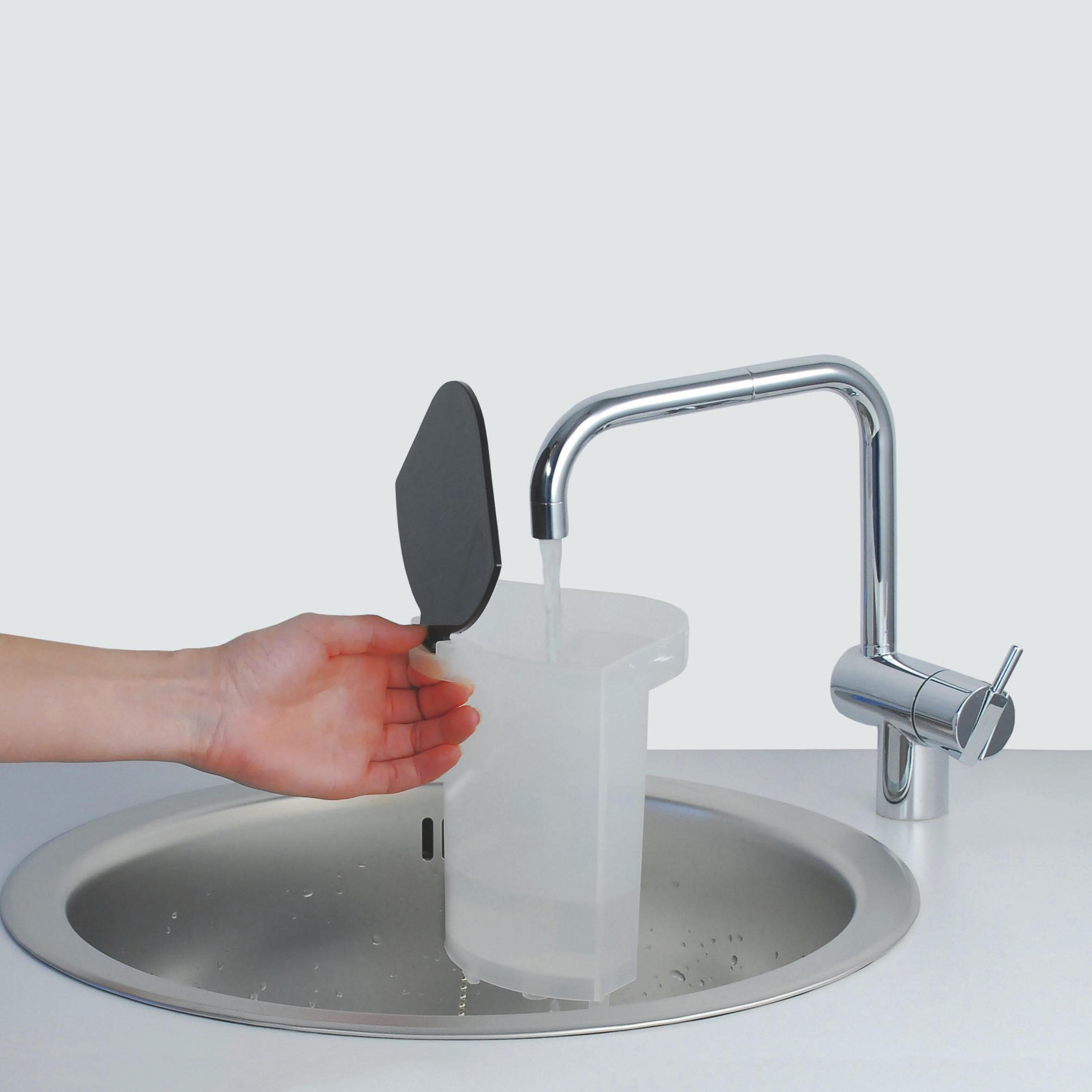 Una mano tiene il coperchio di un contenitore trasparente sotto un rubinetto d'argento con acqua corrente.