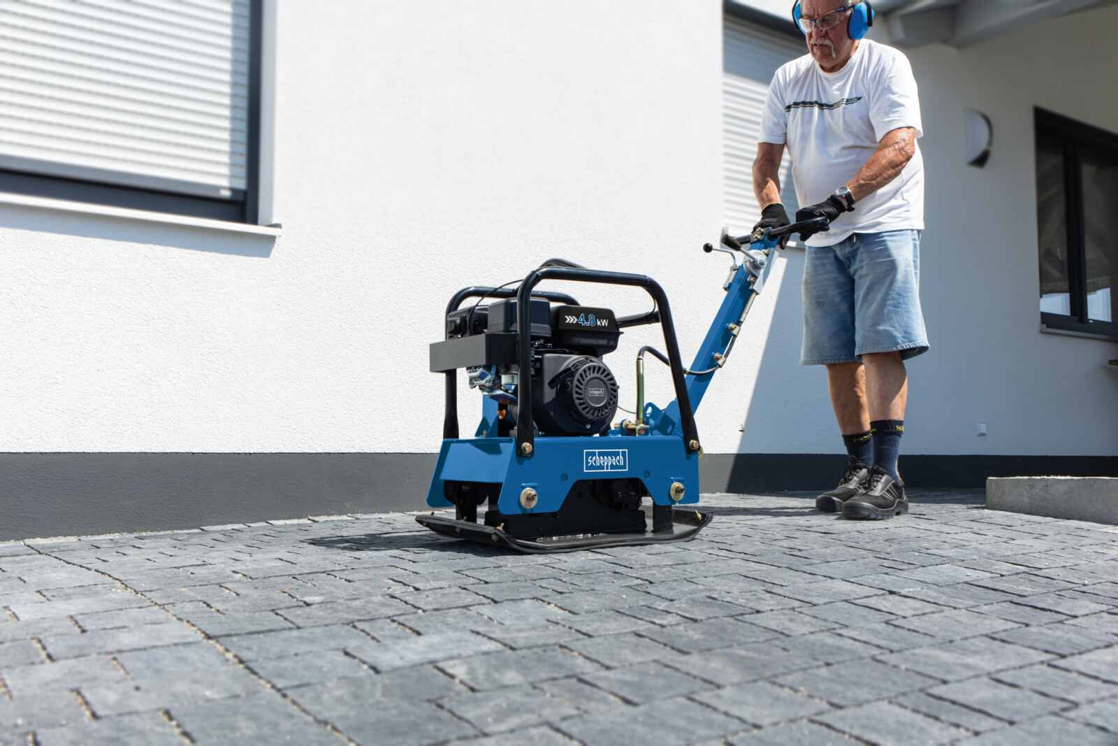 Man gebruikt blauwe verdichtingsmachine op bestraat terras.