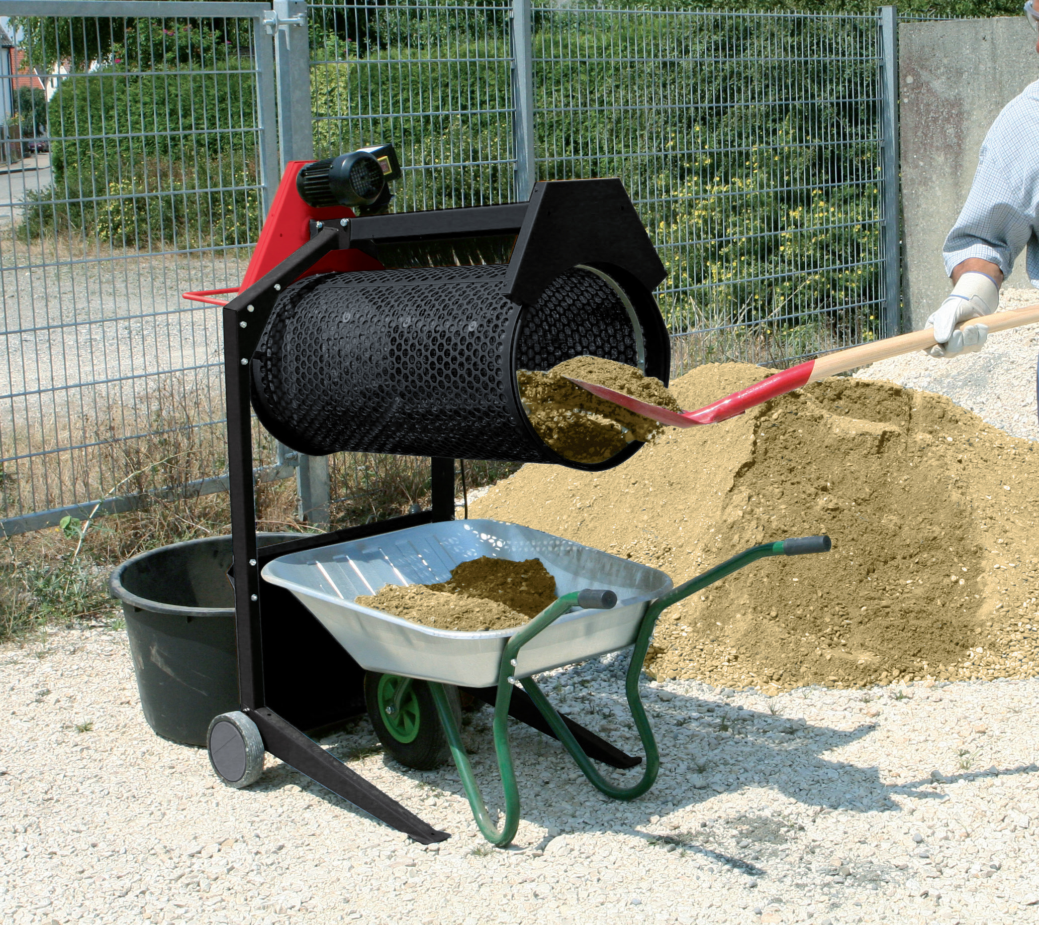 Een machine die zand in een kruiwagen zeeft, met een persoon die een schop gebruikt.