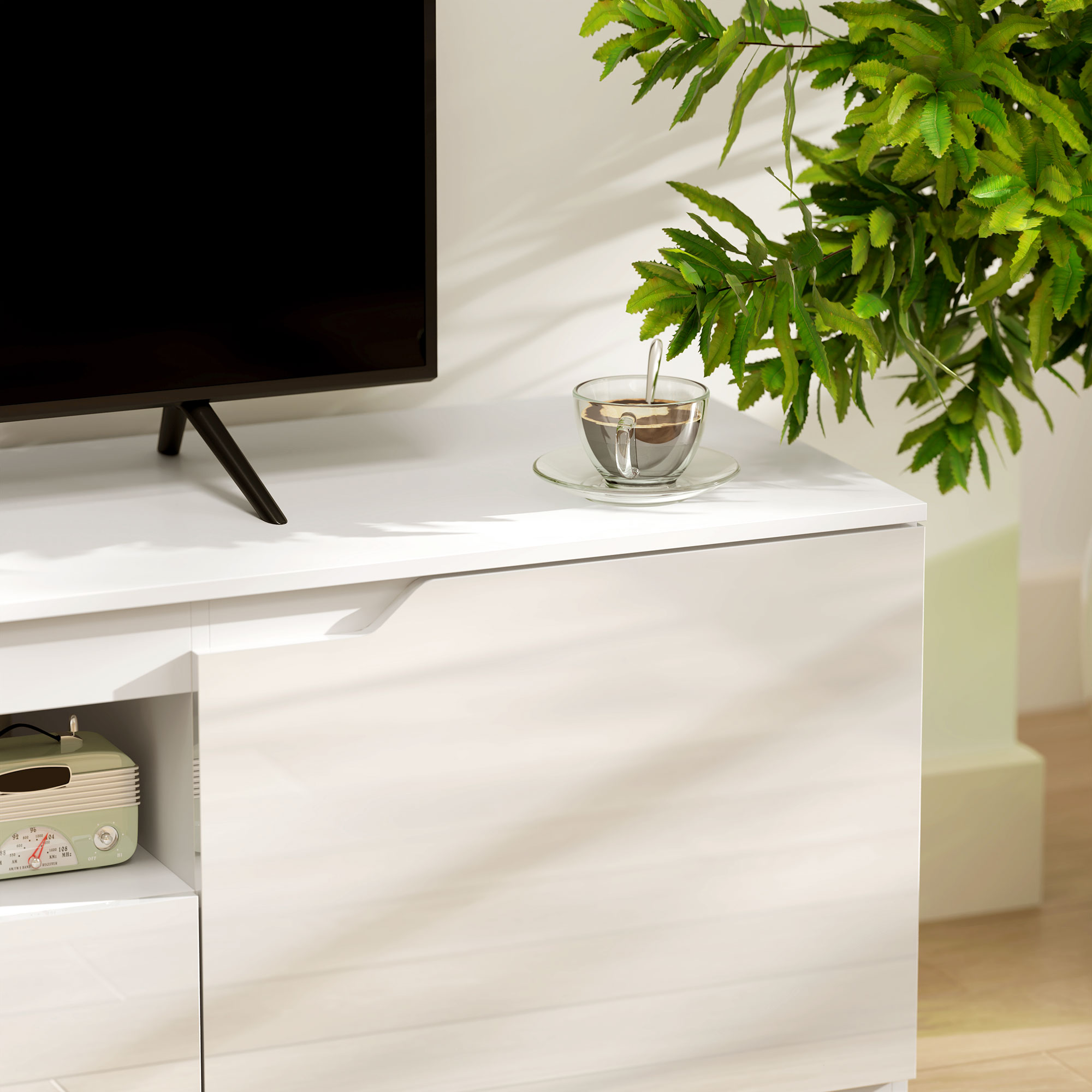 Ein weißer Schrank mit einem schwarzen Fernseher oben drauf. Eine Tasse und eine Pflanze stehen darauf.