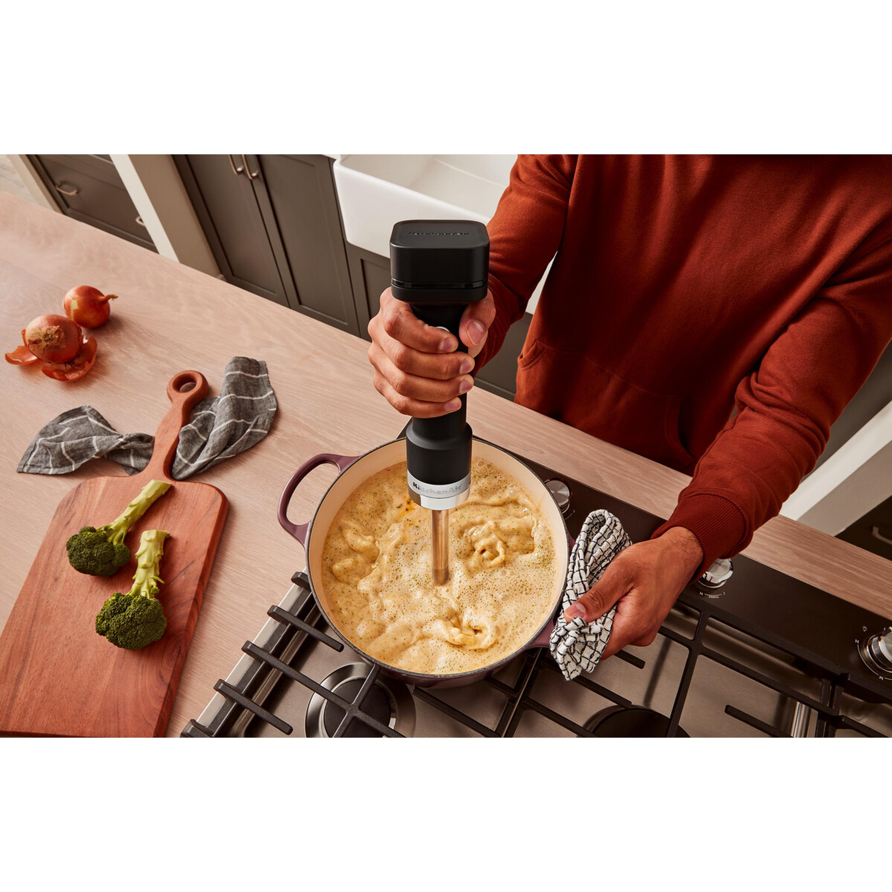 Une personne utilise un mixeur plongeant dans une casserole avec de la nourriture sur une cuisinière.