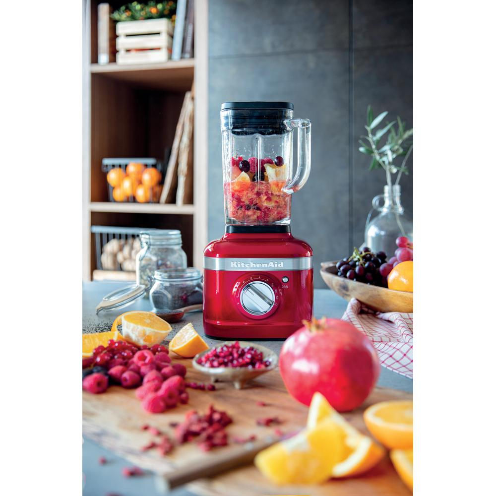 Ahşap kesme tahtası üzerinde kırmızı KitchenAid blender ve meyve malzemeleri.
