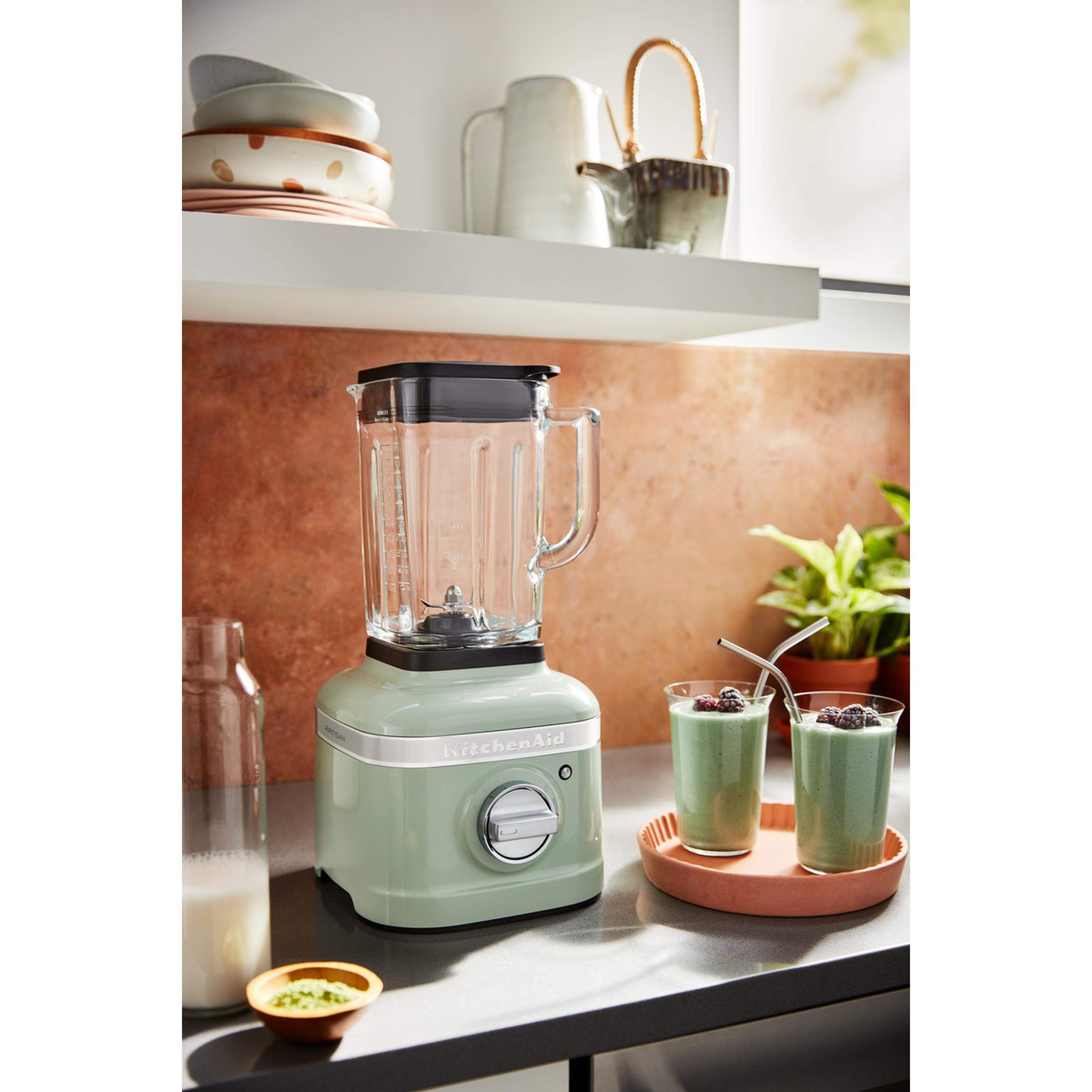 Green blender, two green smoothies, and a bottle of milk on a kitchen counter.