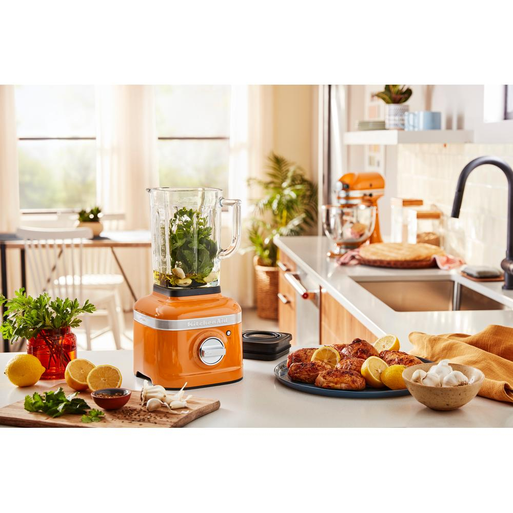 Orange KitchenAid blender on counter with ingredients and other appliances.
