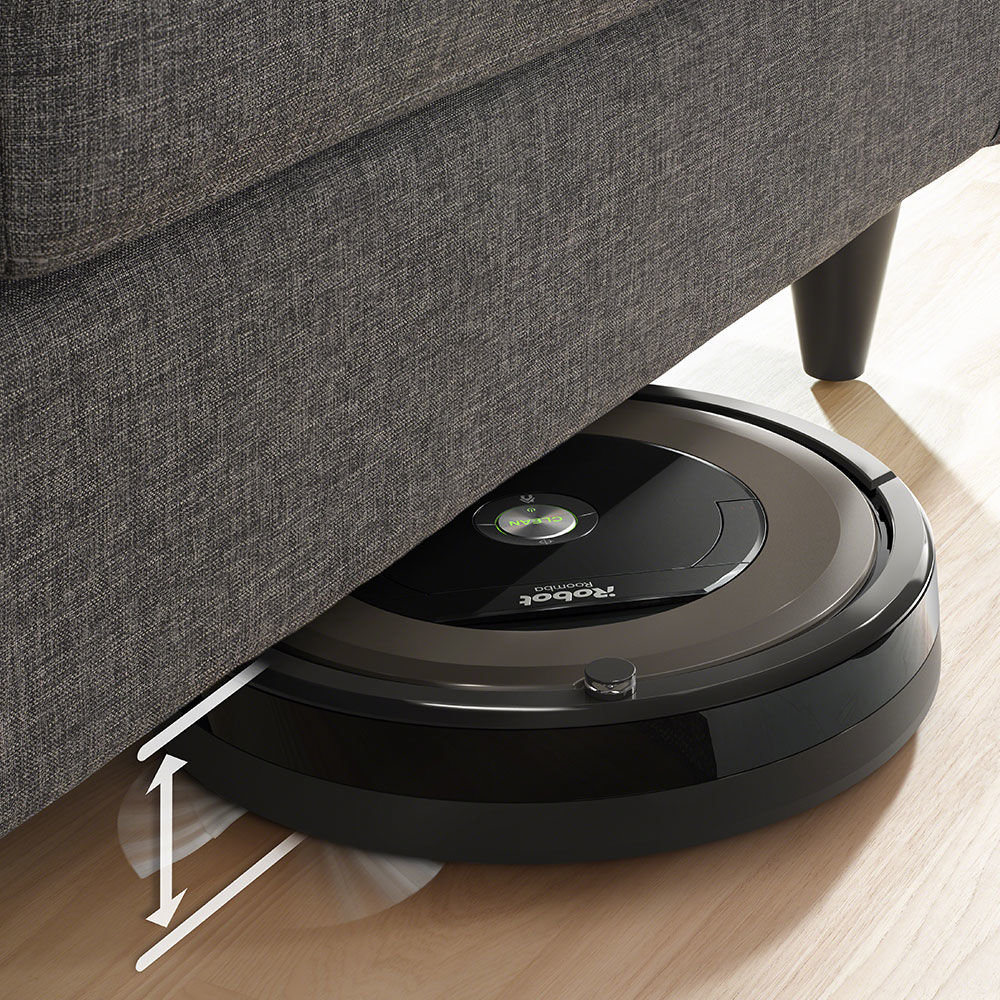Un aspirapolvere Roomba nero sotto un divano grigio, pulisce un pavimento in legno.