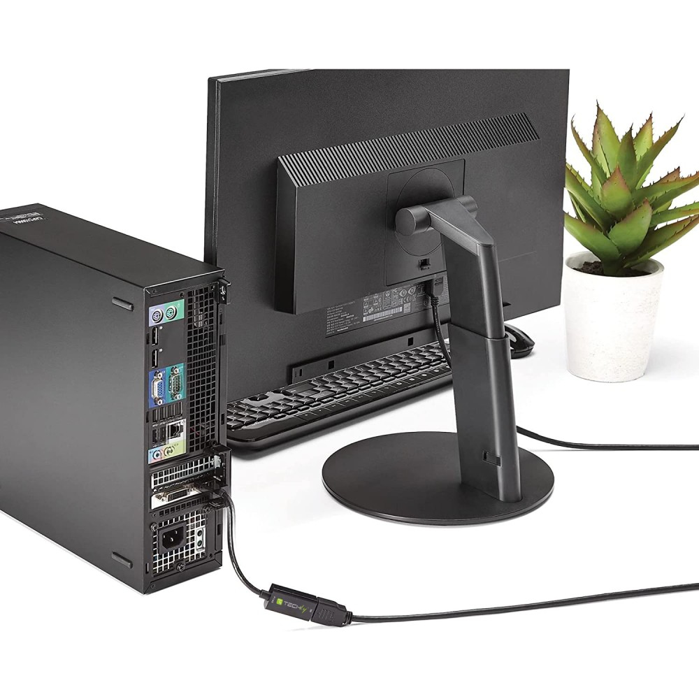 Una computadora conectada a un monitor mediante un cable, con una pequeña planta a la derecha.