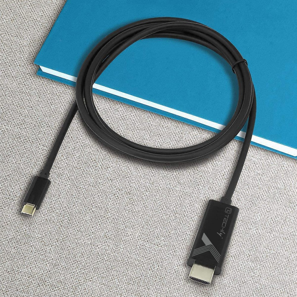 Cable USB-C negro enrollado sobre superficie gris con cuaderno azul al fondo.