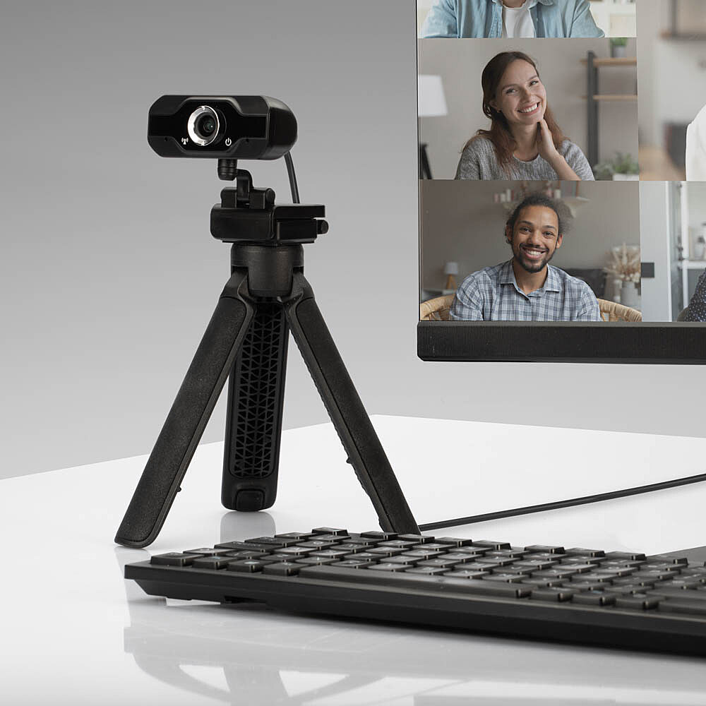 Webcam su un treppiede, tastiera e monitor. Videochiamata con persone nel monitor. Sfondo bianco.