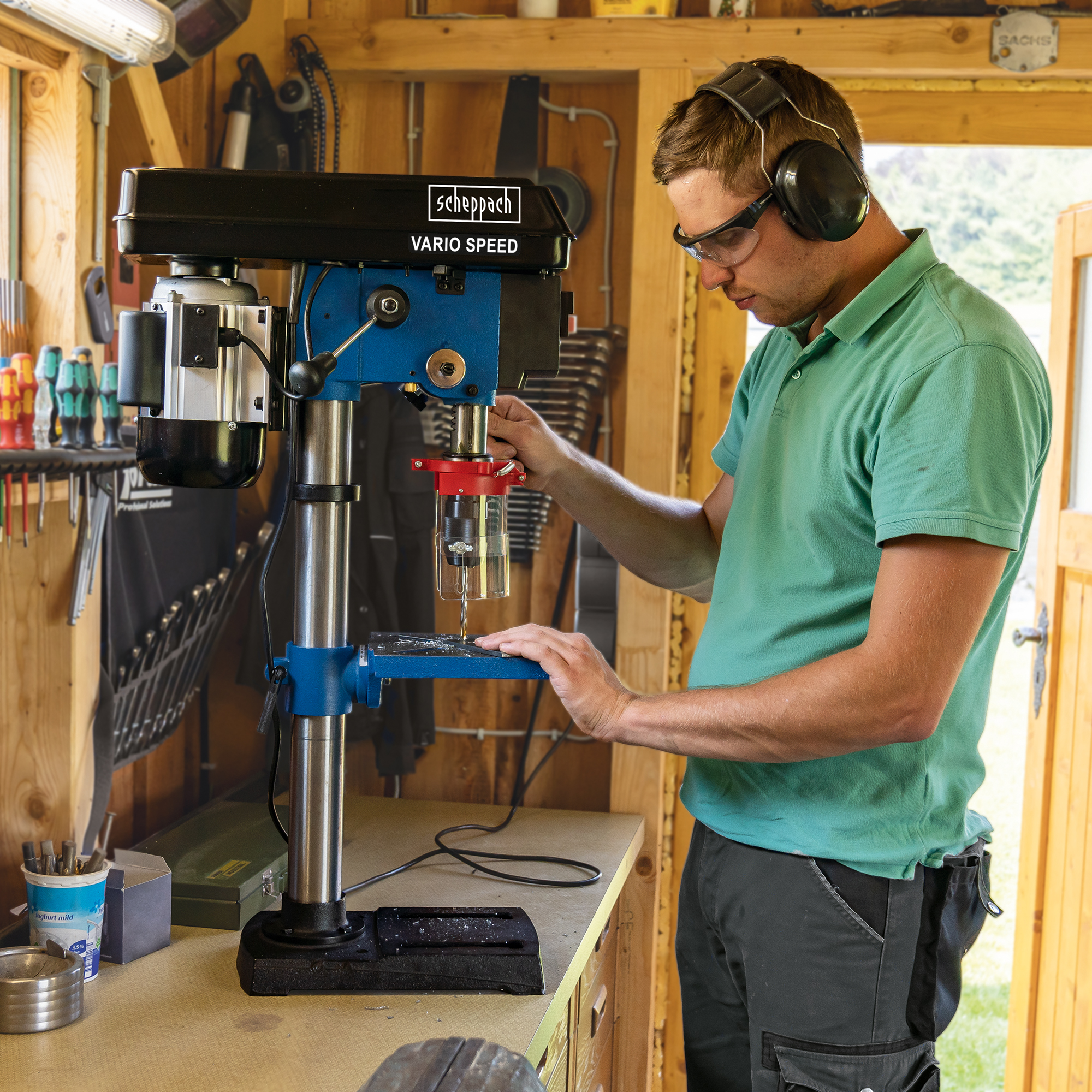 Ein Mann in einer Werkstatt bohrt Holz mit einer blau-schwarzen Bohrmaschine.