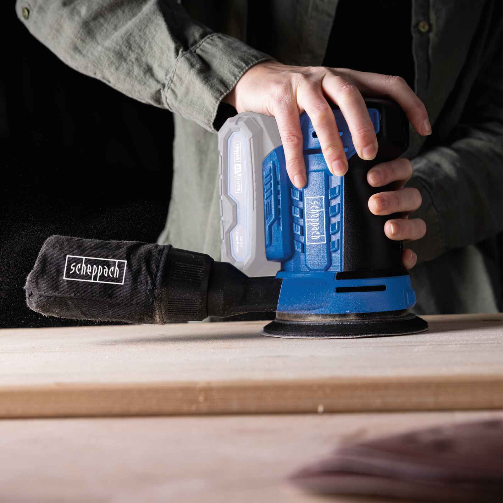 Una persona usa una levigatrice blu e nera su una superficie di legno.
