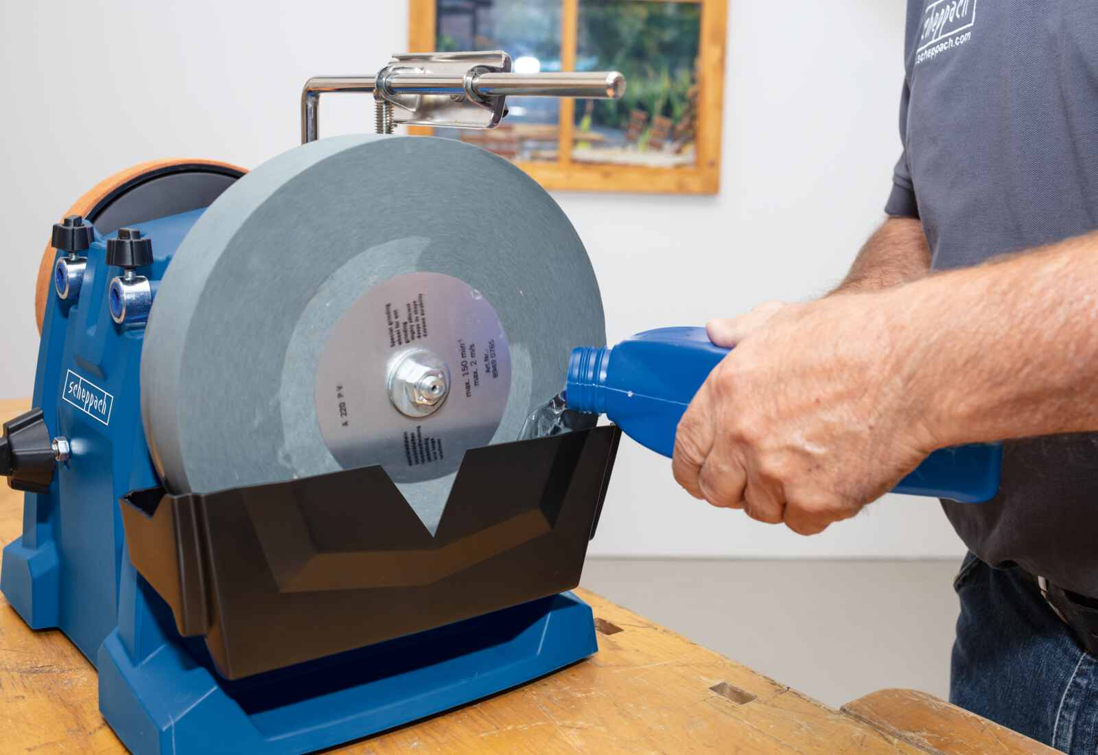 Una persona versa liquido blu da una bottiglia su una mola, un banco da lavoro è in primo piano.