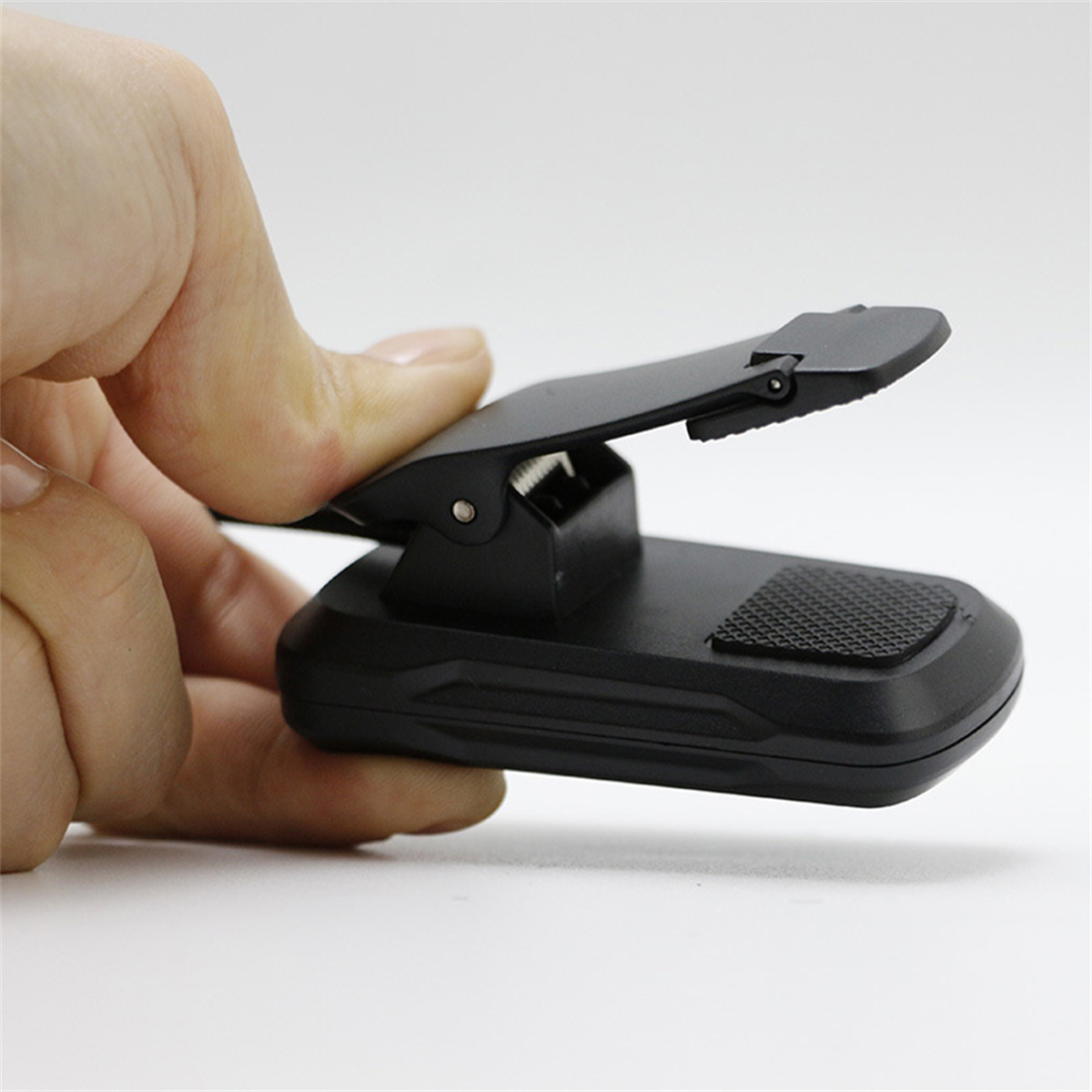Eine Hand hält eine schwarze Clip-on-Leselampe und zeigt den geöffneten Clip, der die Basis der Lampe freilegt.