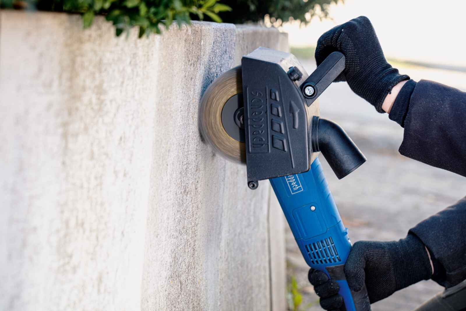 Una persona usa una smerigliatrice blu e nera su un muro di cemento, le scintille volano.