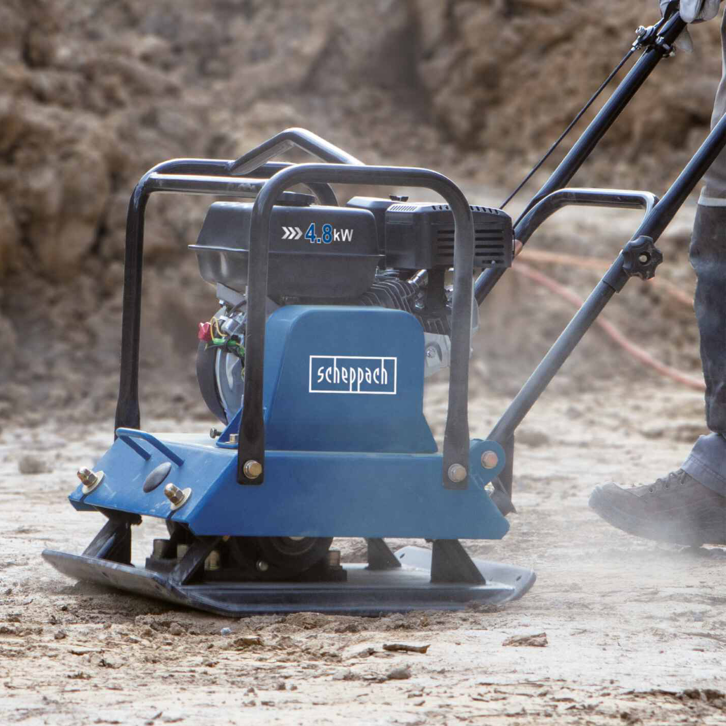 Un compattatore a piastra Scheppach blu sta compattando il terreno in un cantiere.